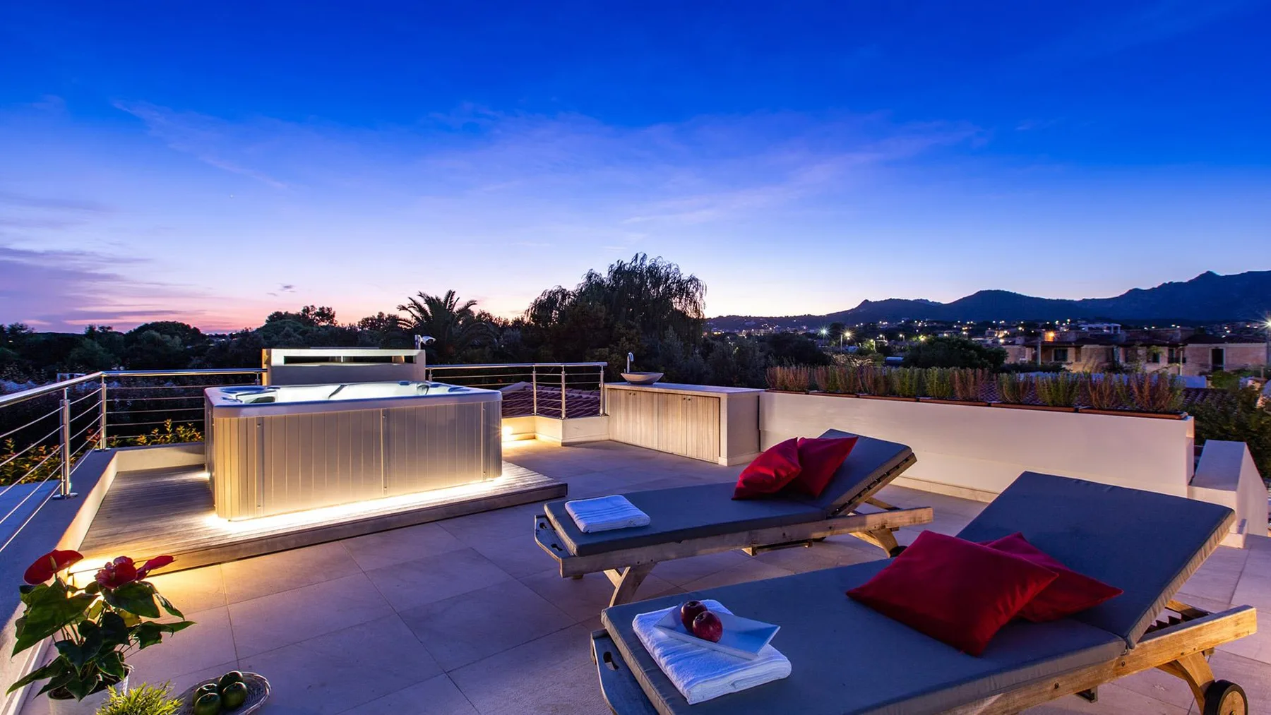 Una terraza en la azotea tiene asientos, una mesa baja y una barra iluminada al atardecer.