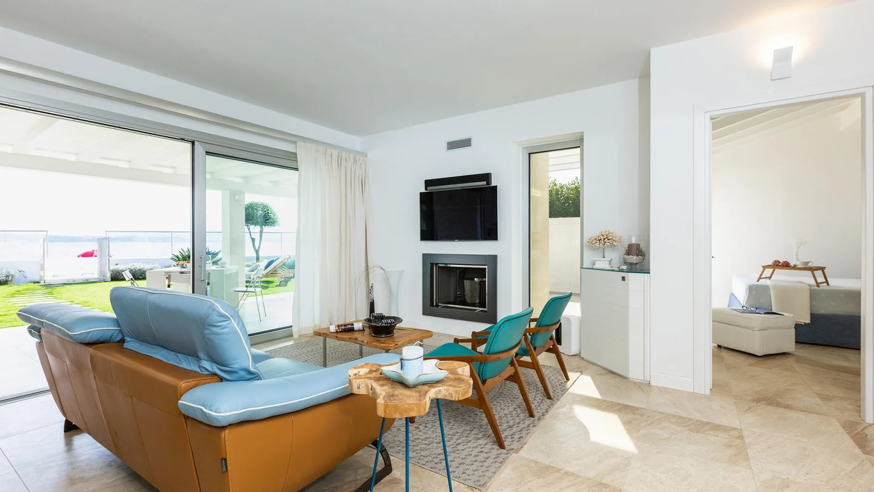 Una sala luminosa con asientos, un televisor y puertas corredizas de vidrio que dan a un patio.