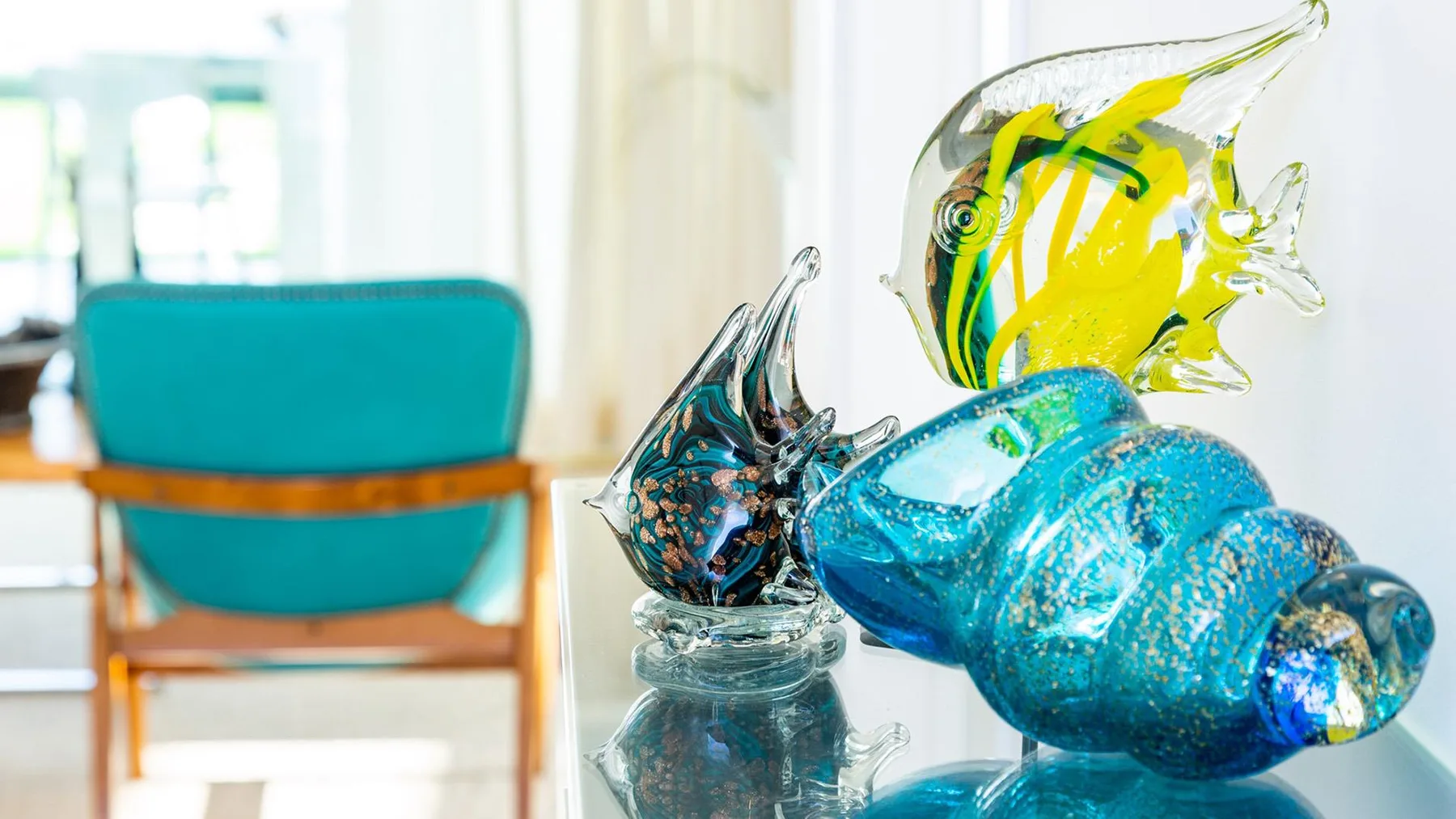 Peces decorativos de vidrio están sobre una mesa en una habitación luminosa.