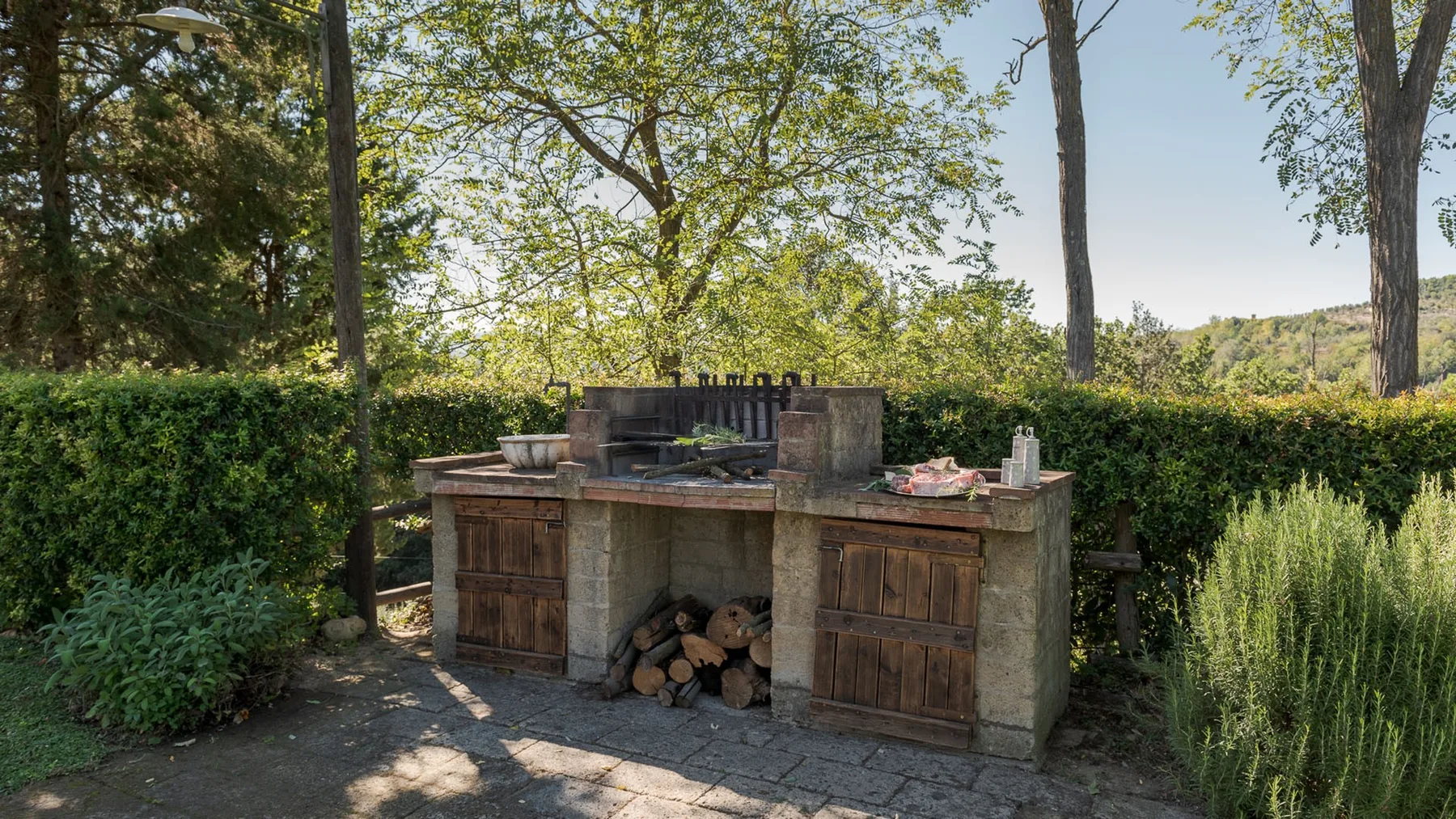 Una zona de cocina al aire libre con una parrilla empotrada y leña bajo la encimera.
