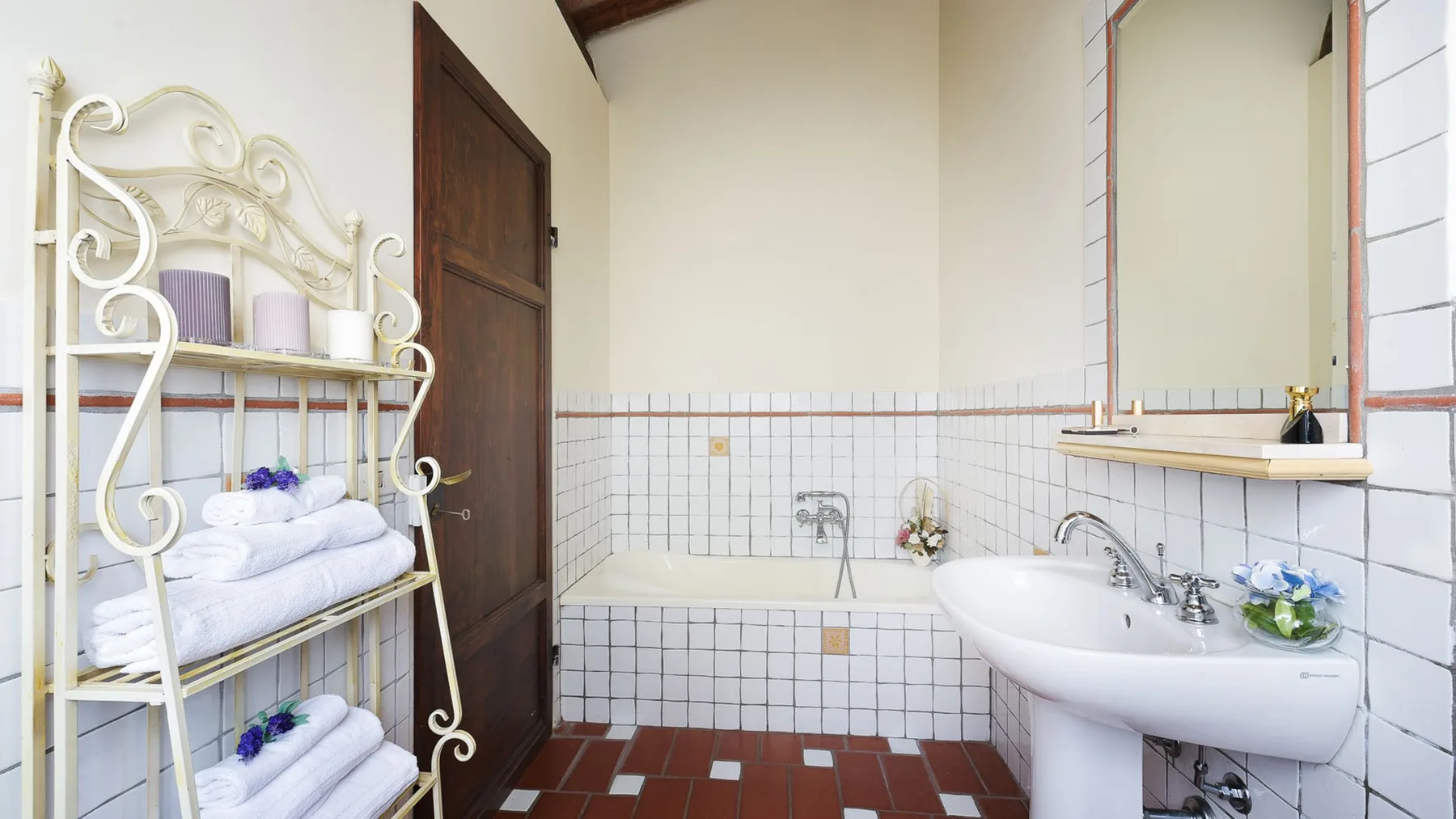 Un baño con azulejos, lavabo, espejo de pared y toallas dobladas en un estante.