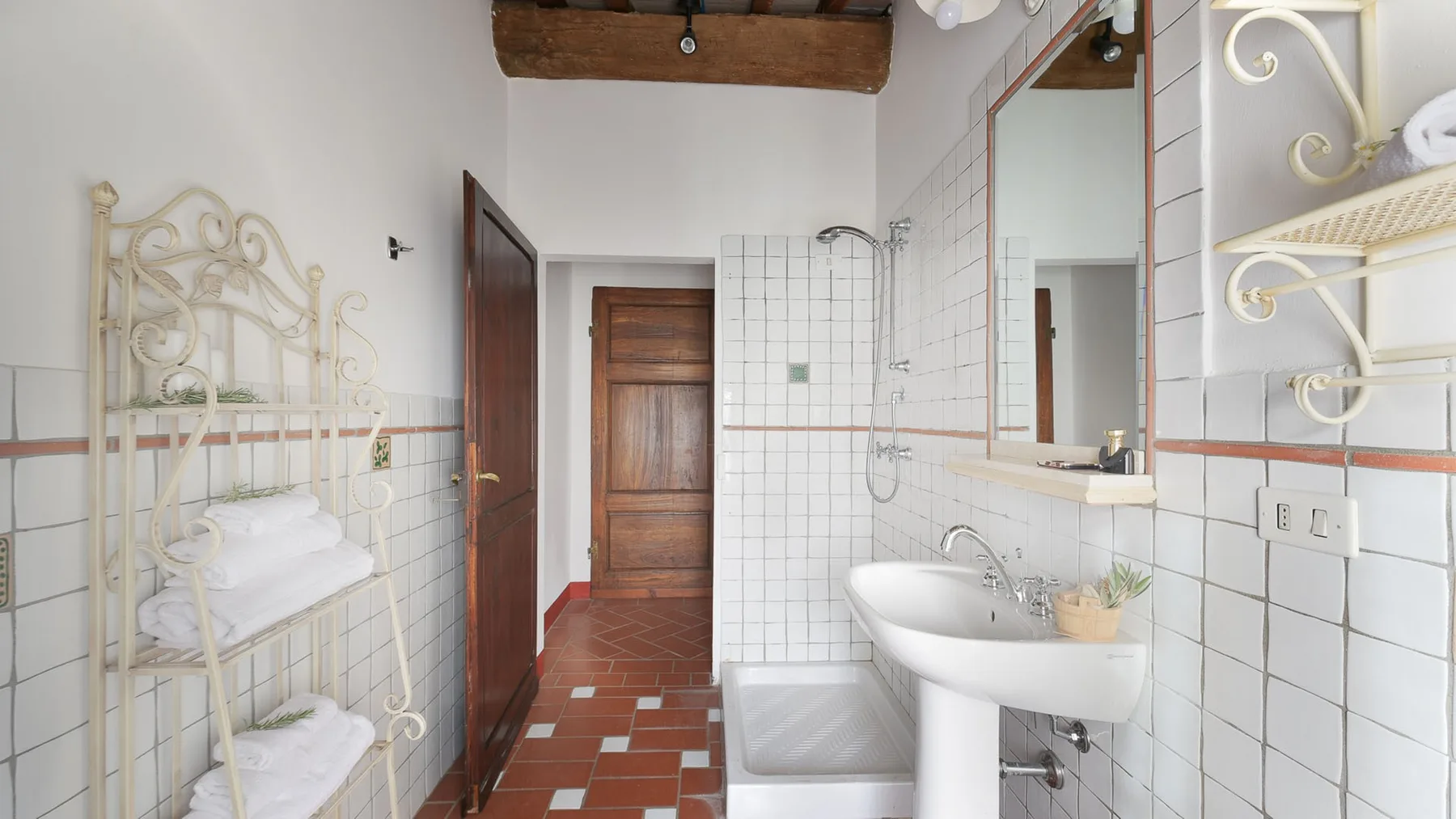 Un baño alicatado con lavabo, ducha y toallas dobladas en un estante.
