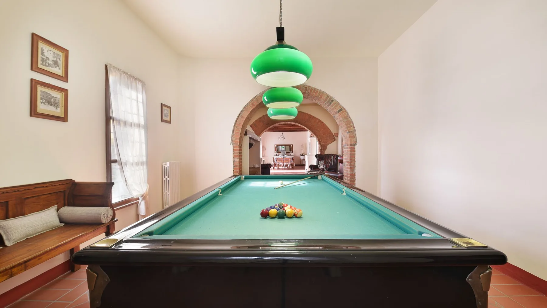Una sala de billar con una mesa bajo lámparas colgantes verdes.