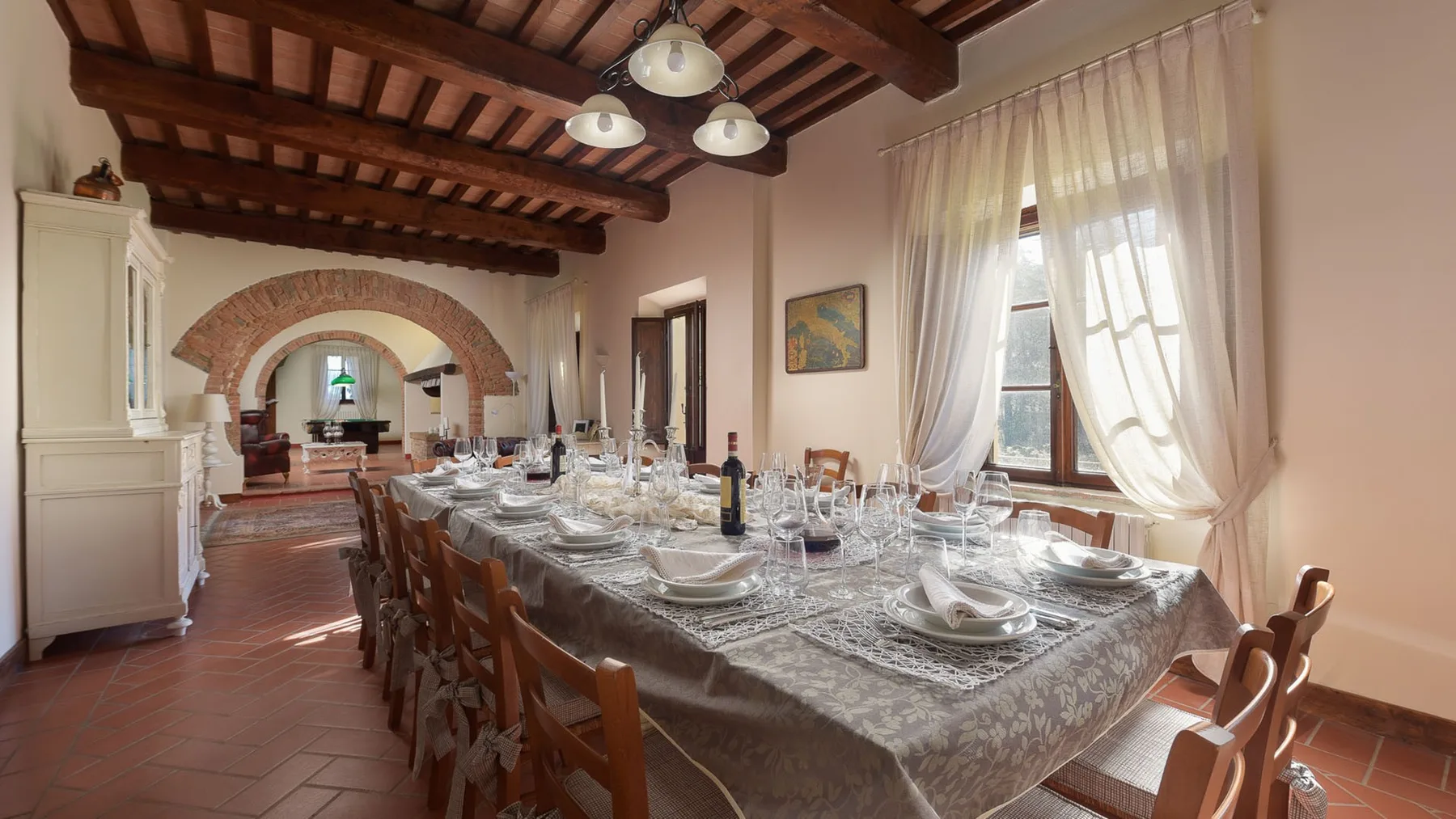 Un comedor con una mesa larga preparada con vajilla bajo vigas de madera a la vista.