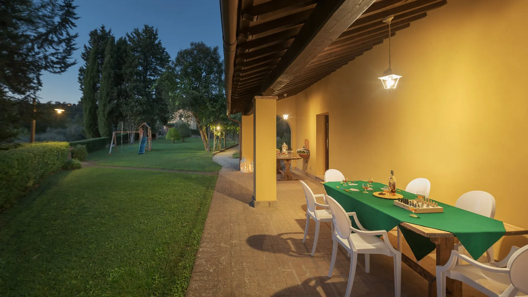 Comedor exterior cubierto con una mesa verde junto a un jardín ajardinado.