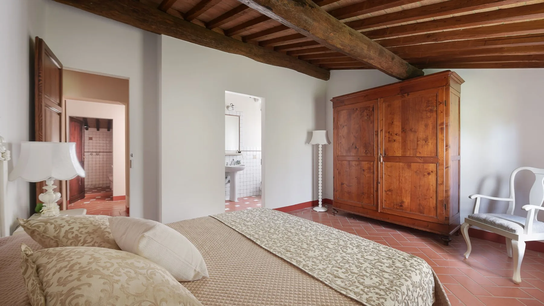 Un dormitorio con una colcha estampada, un armario de madera y vigas expuestas en el techo.