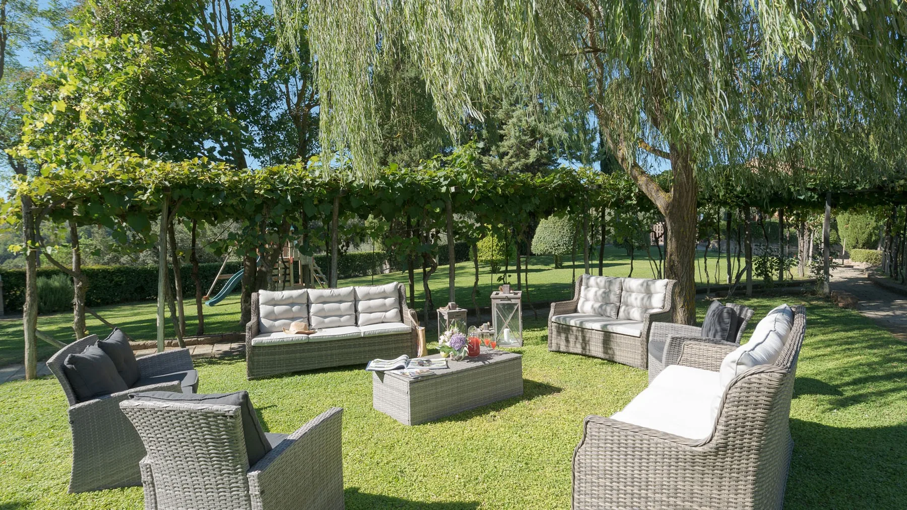 Una zona de estar al aire libre con muebles de mimbre bajo árboles frondosos.