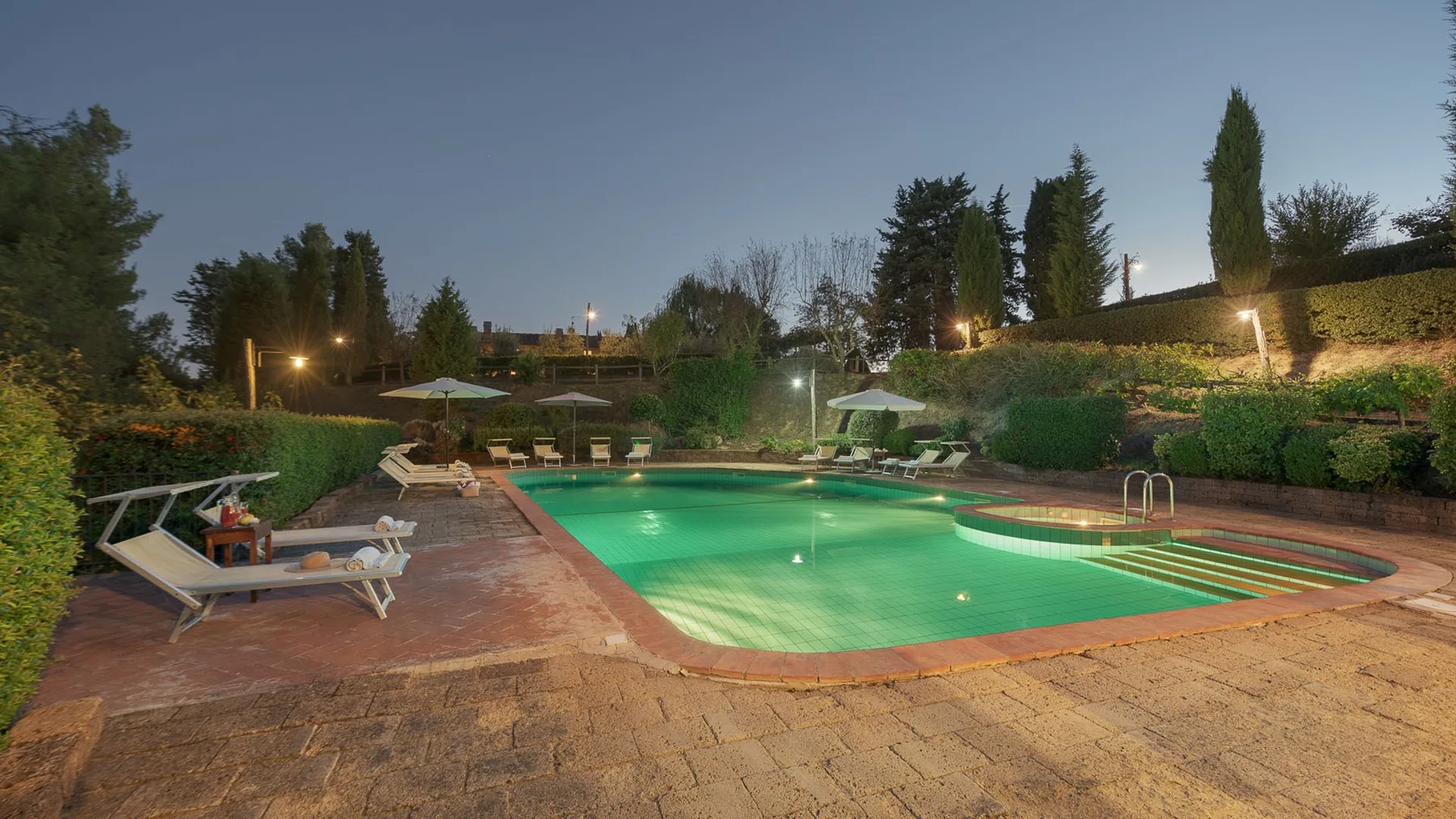 Una piscina al aire libre está rodeada de una terraza pavimentada y asientos reclinables.