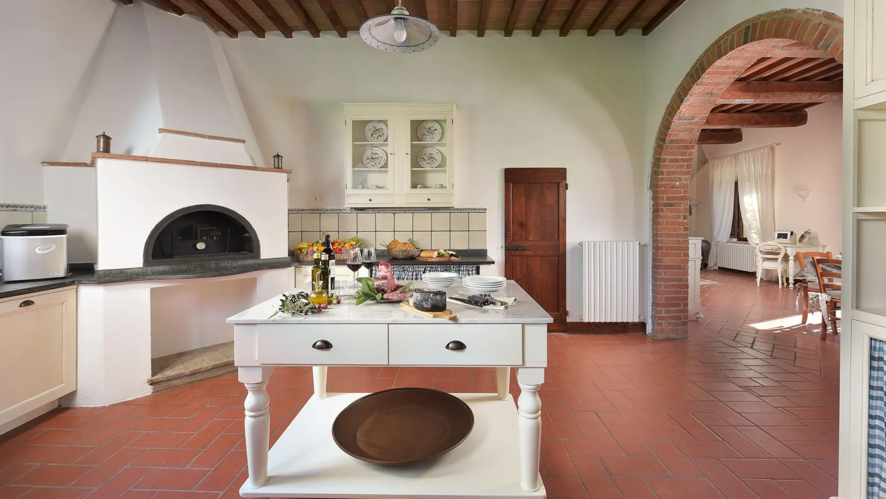 Una cocina amplia con una mesa central, una chimenea y un arco de ladrillo.