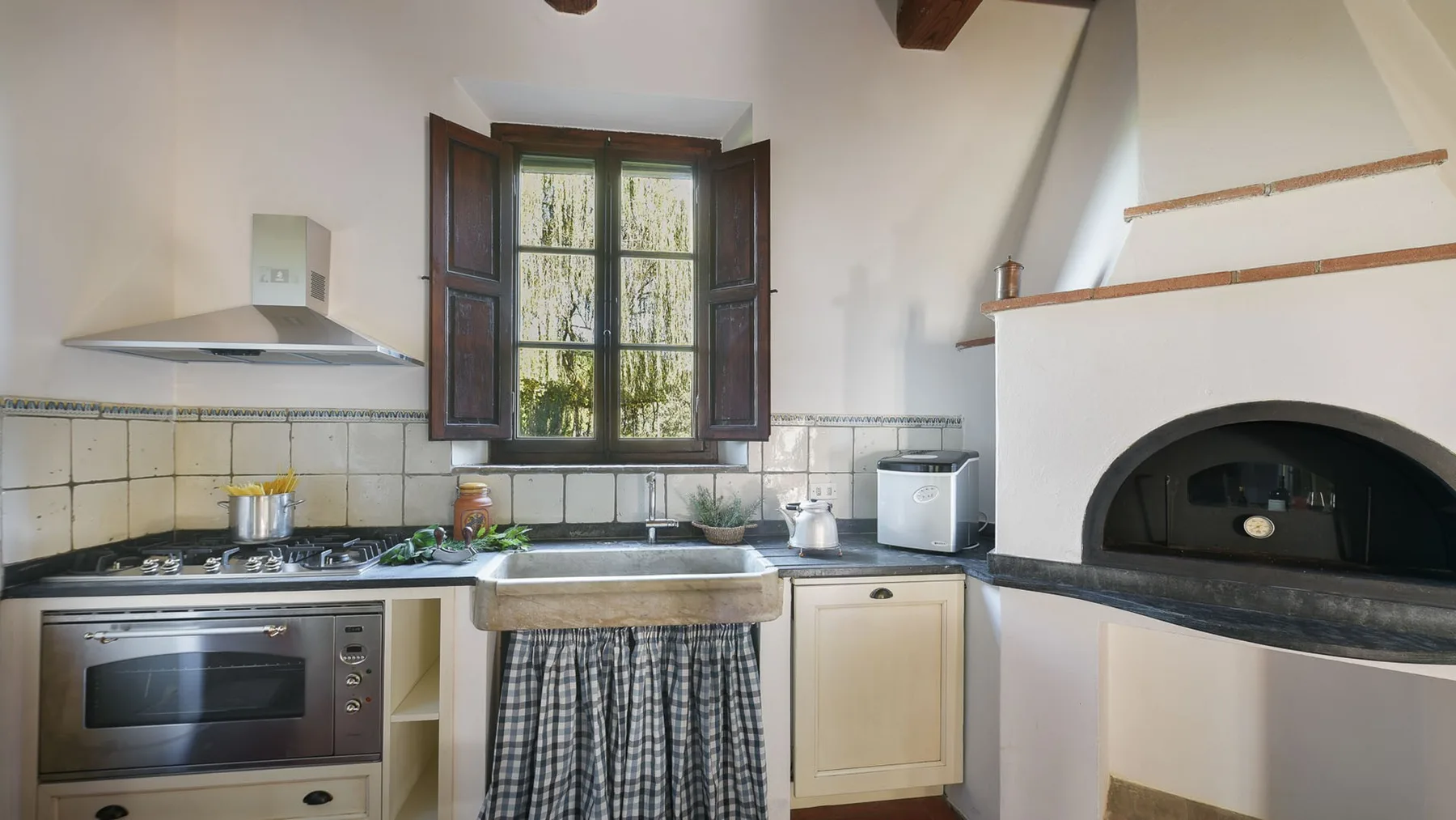 Una cocina con una ventana central, horno empotrado y una gran chimenea arqueada.
