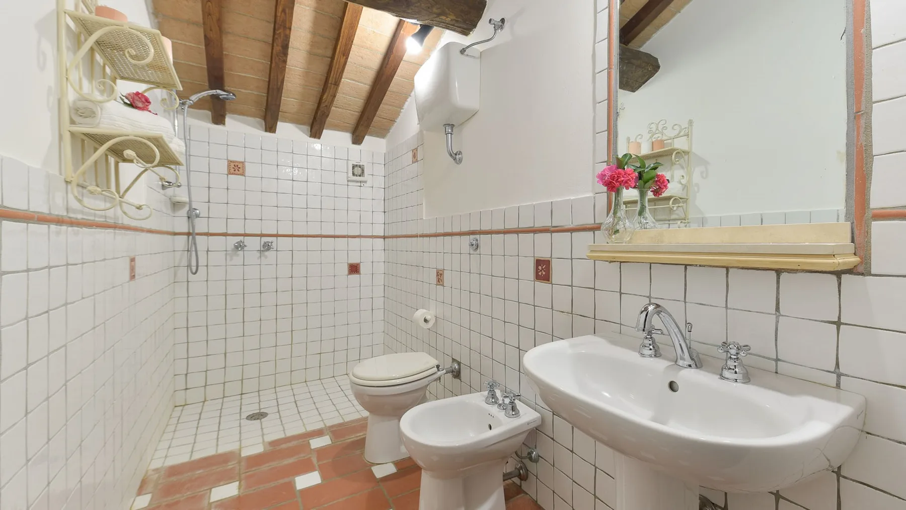 Un baño con azulejos, bañera, lavabo e inodoro bajo vigas de madera expuestas.