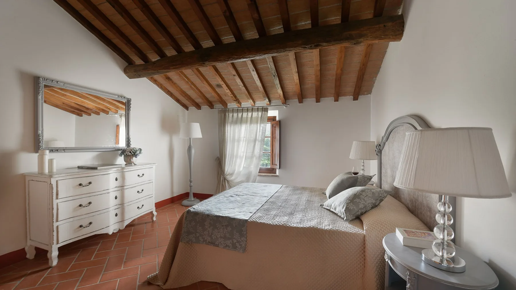 Un dormitorio con una cama, una cómoda y vigas de madera expuestas en el techo.