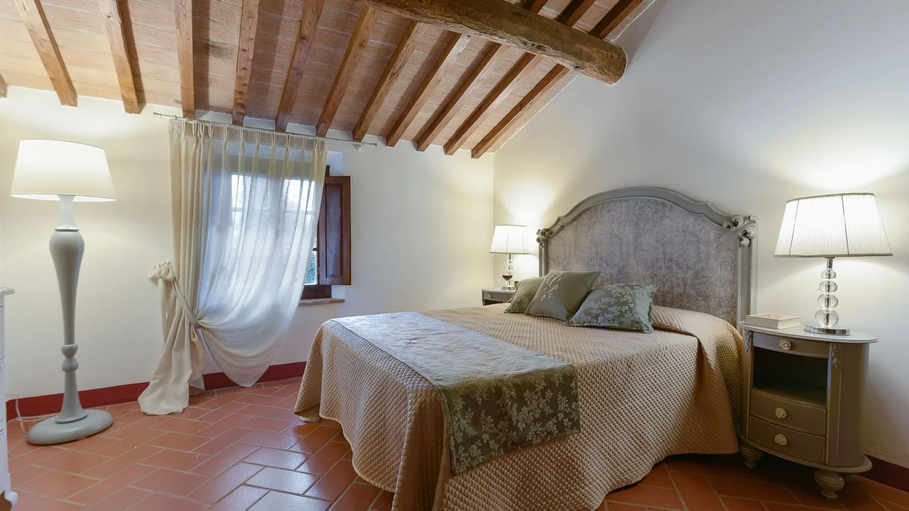Un dormitorio con una cama doble, mesitas de noche y una ventana bajo un techo con vigas de madera.