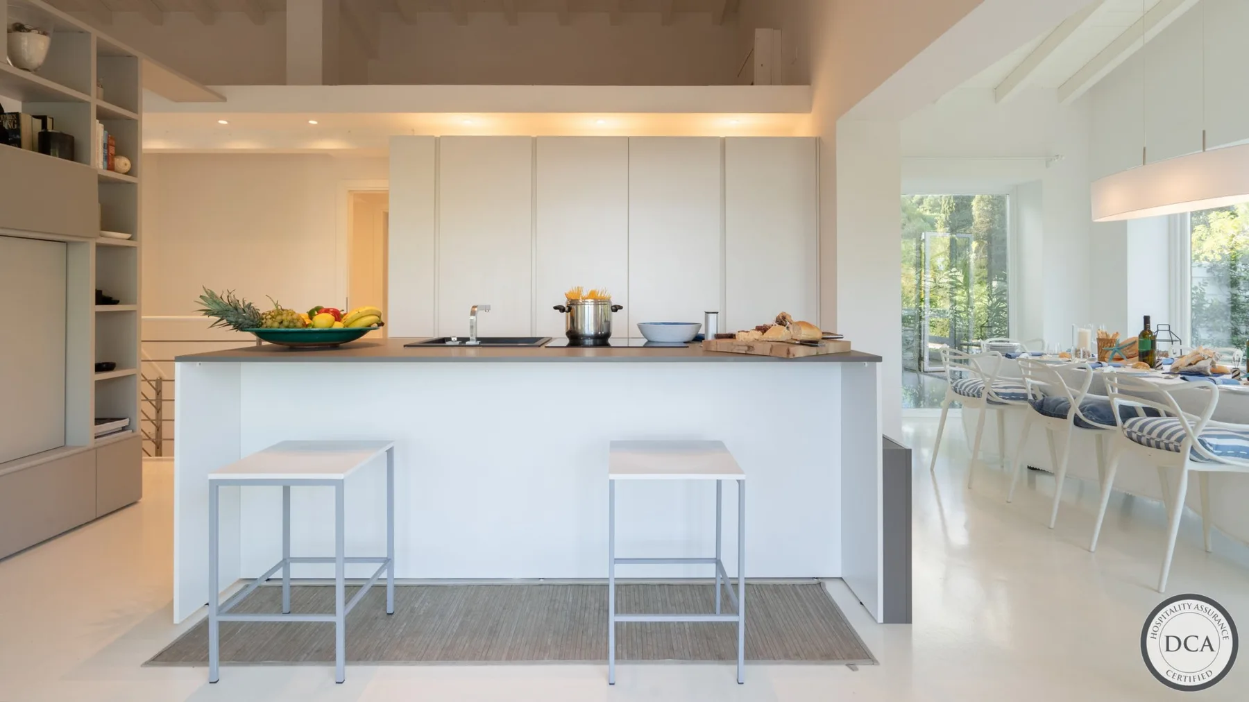 A bright kitchen with a central island and stools, opening onto a dining area.
