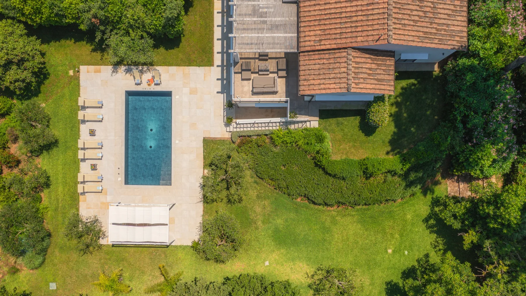 An aerial view shows a rectangular swimming pool beside a tiled patio and house.