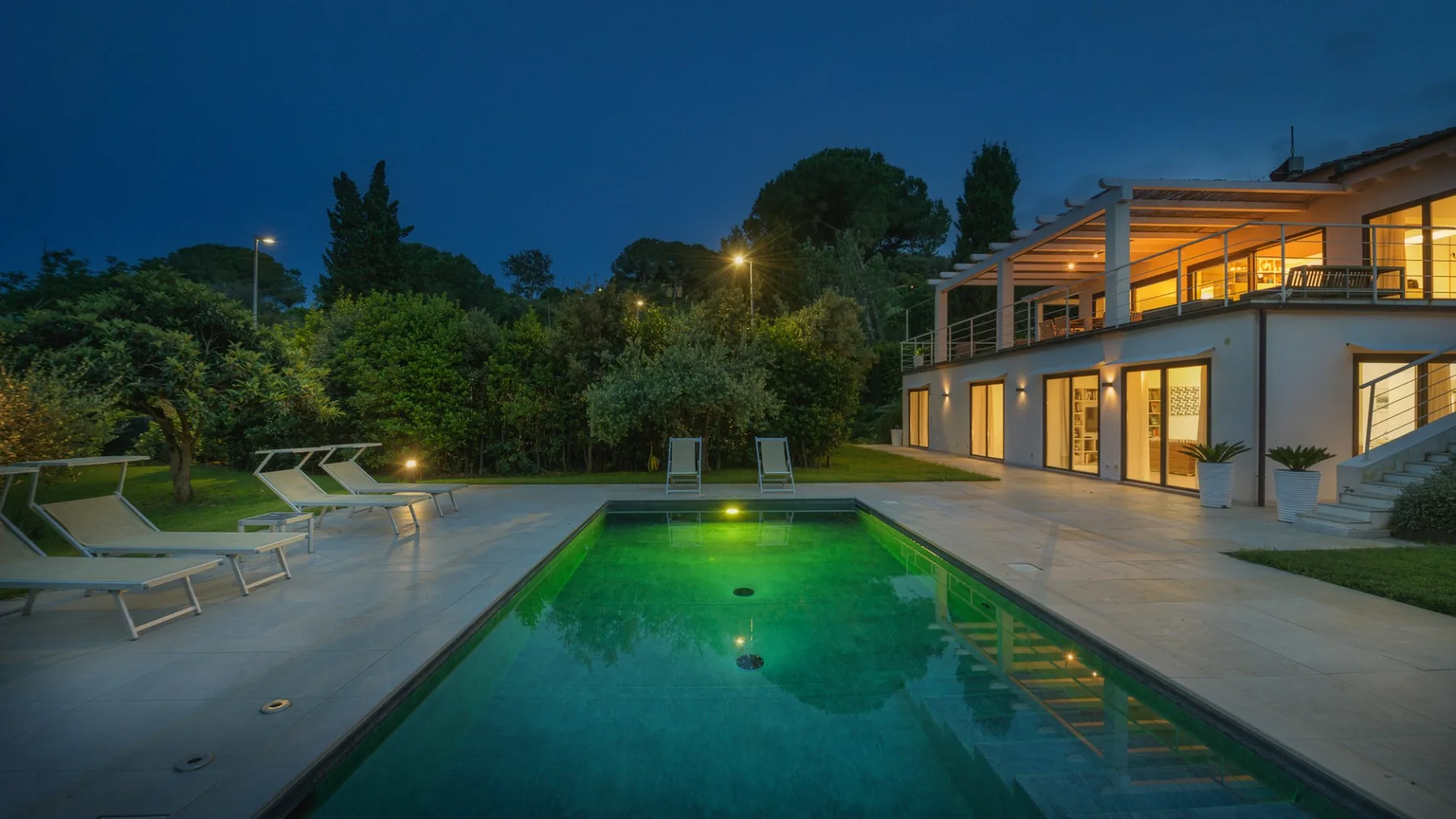 An outdoor pool beside a modern house glows under evening lights.
