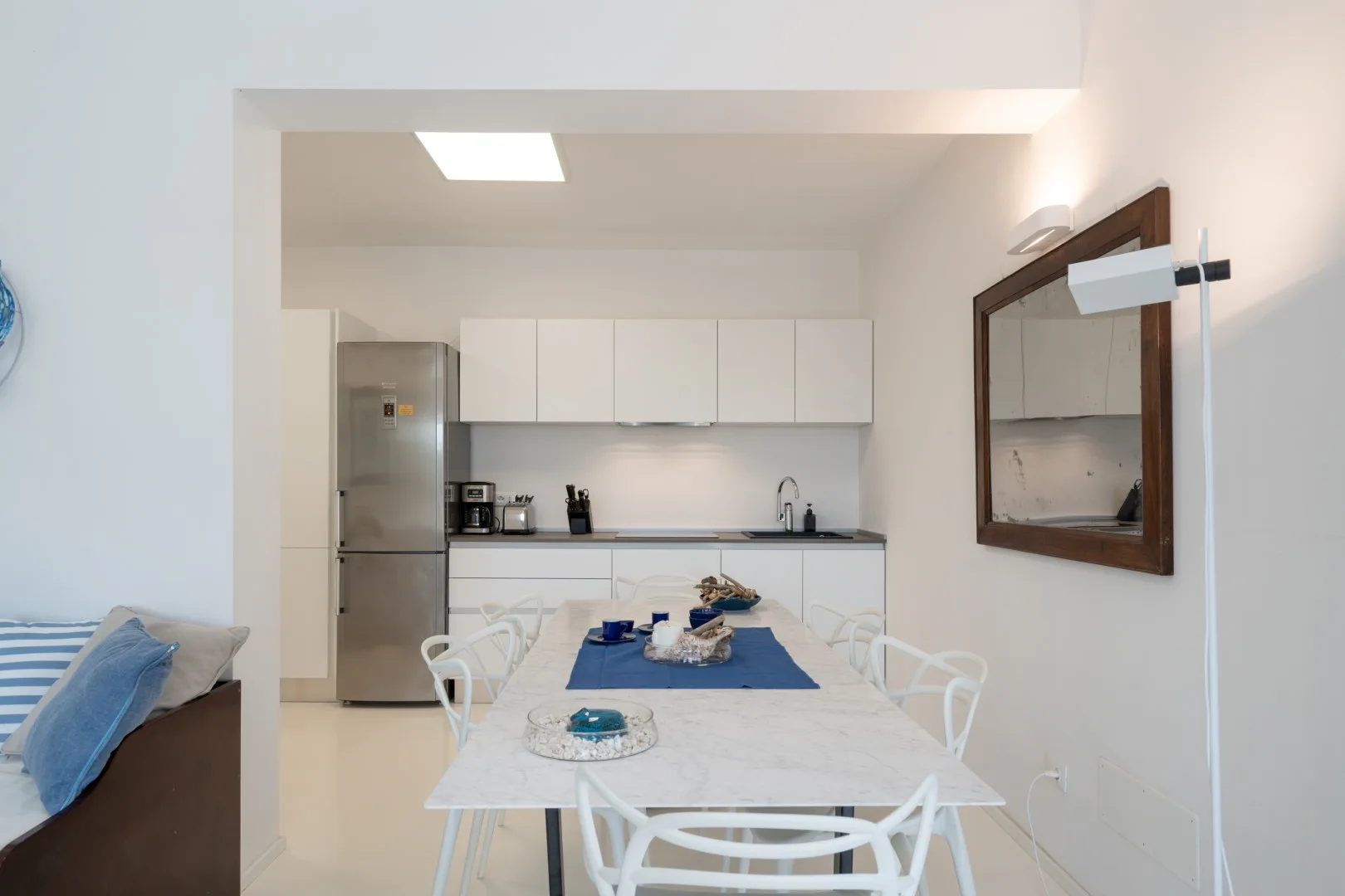 A dining area opens into a kitchen, with a table and white chairs.
