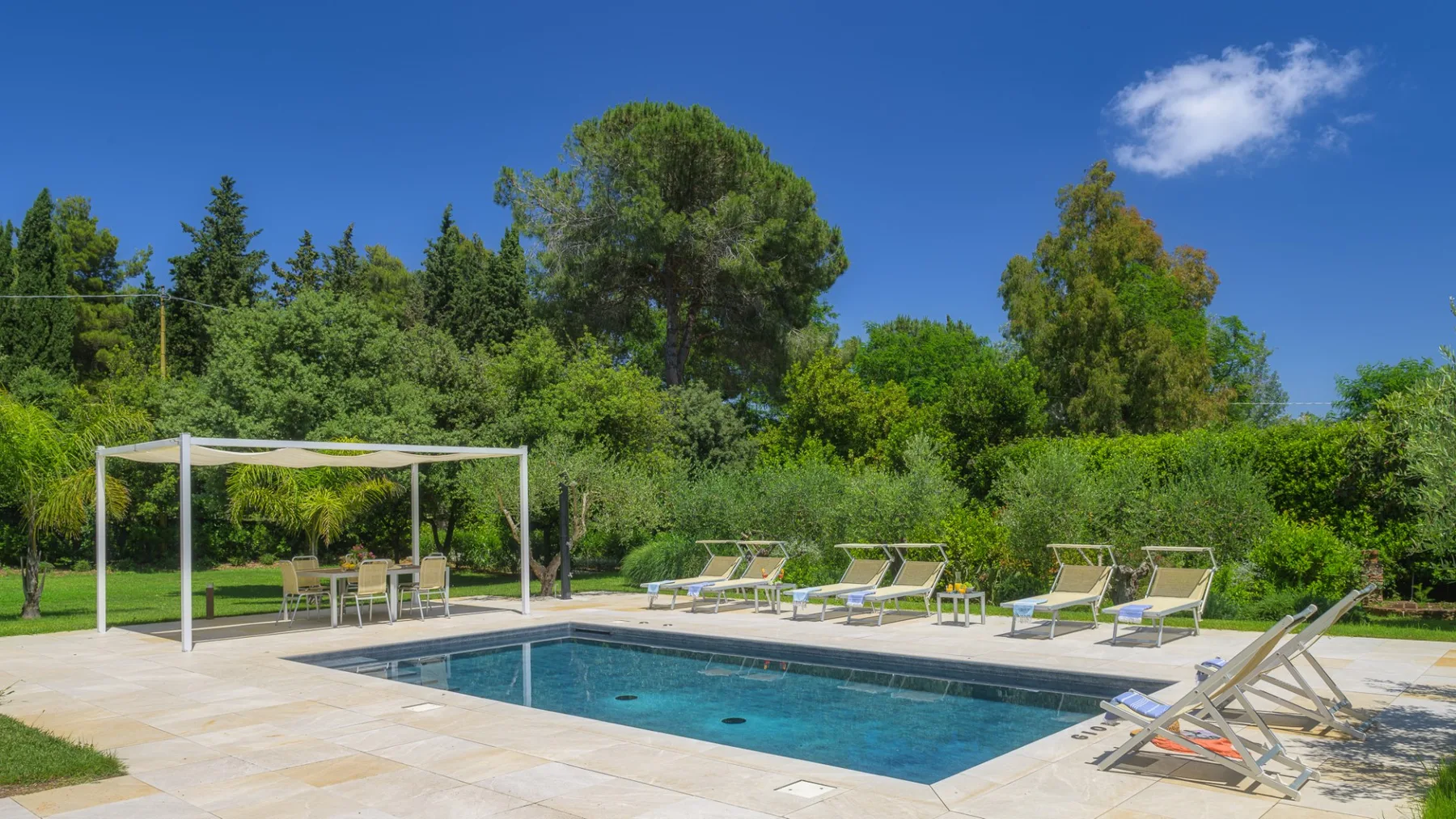 An outdoor swimming pool is surrounded by lounge seating and greenery.