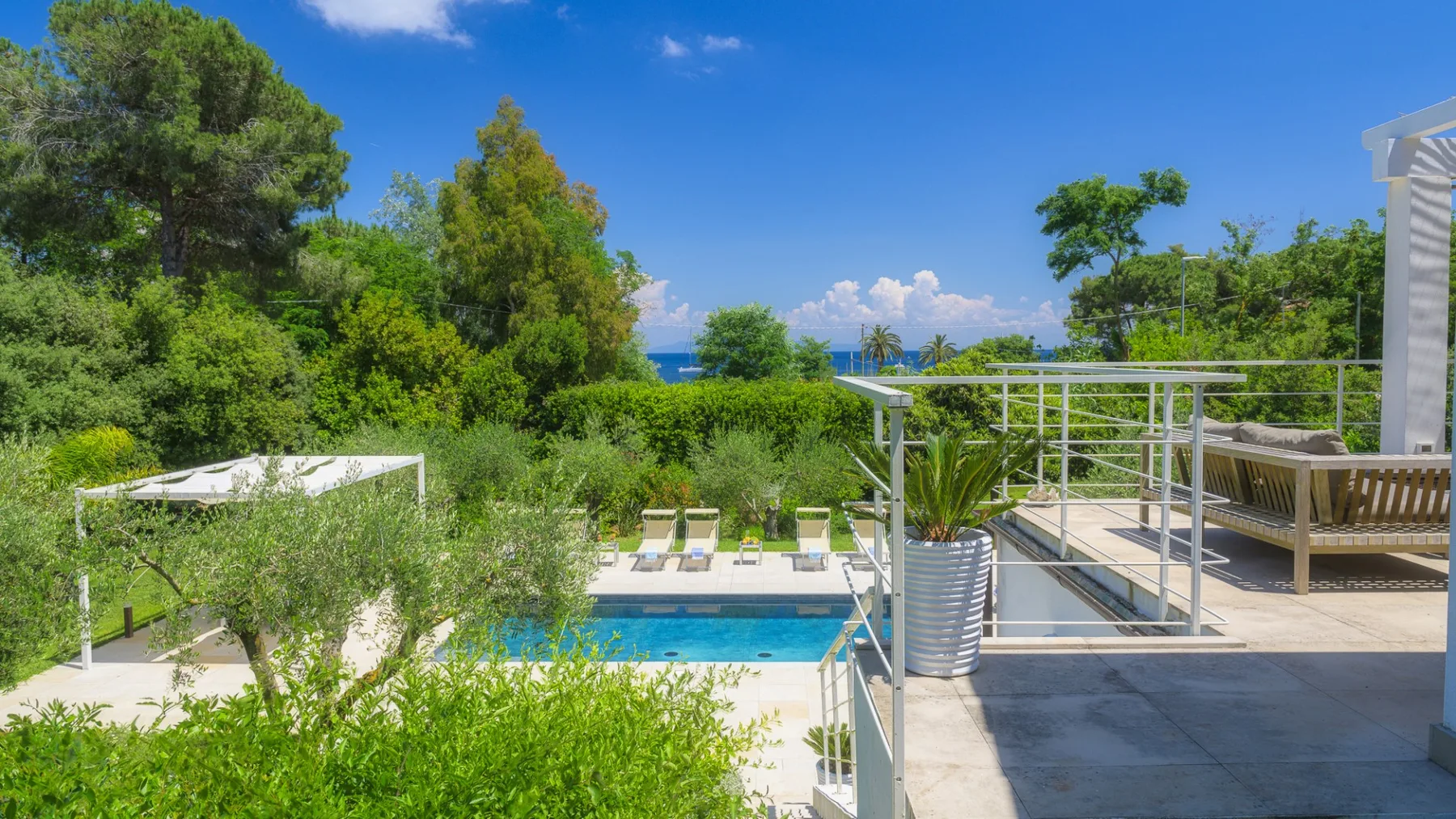 An outdoor pool and terrace overlook dense greenery and a distant blue horizon.