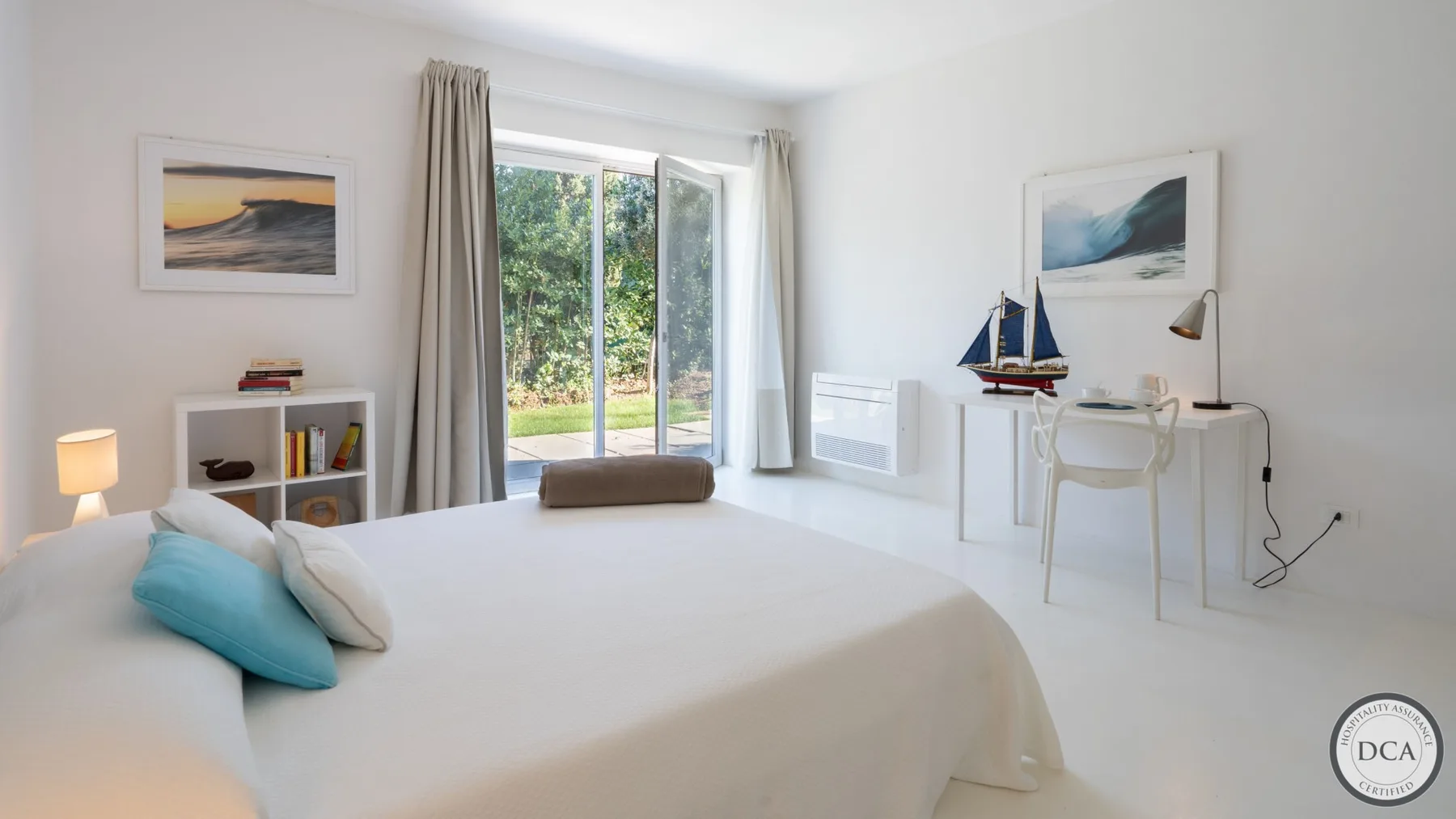 A bright bedroom with a bed, a desk, and glass doors opening onto greenery.