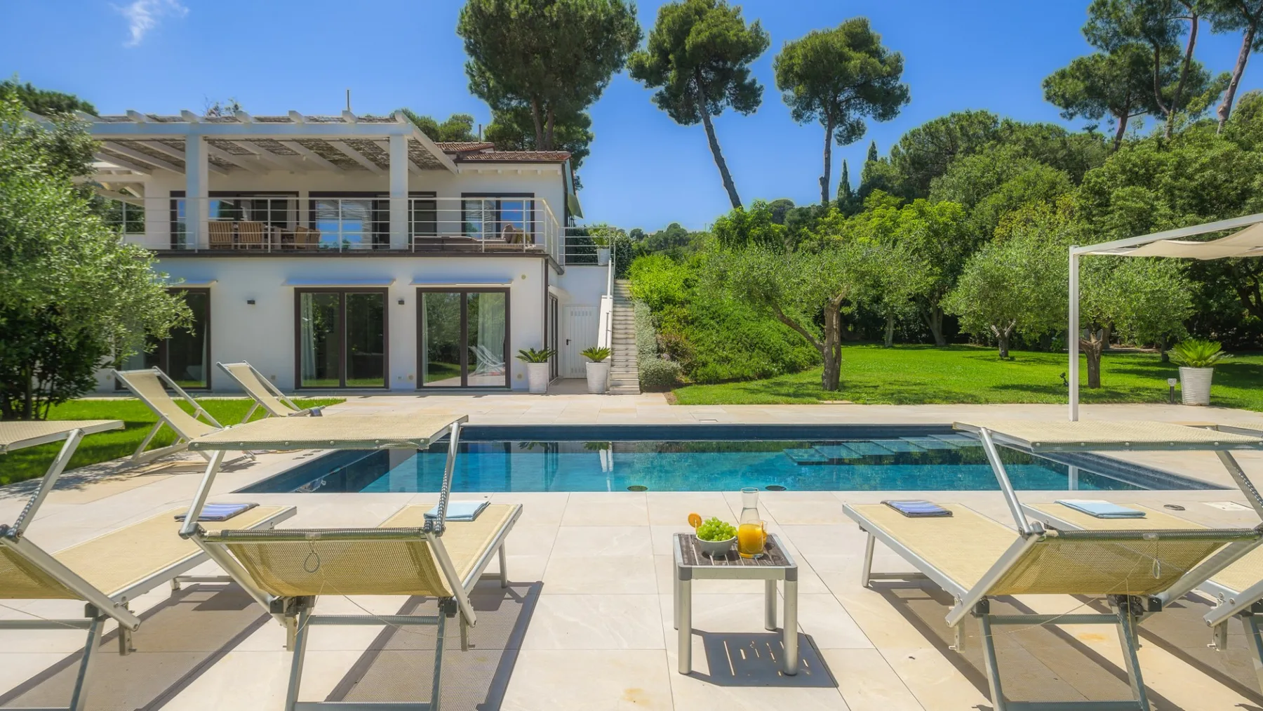A swimming pool and lounge seating sit in front of a modern house and garden.