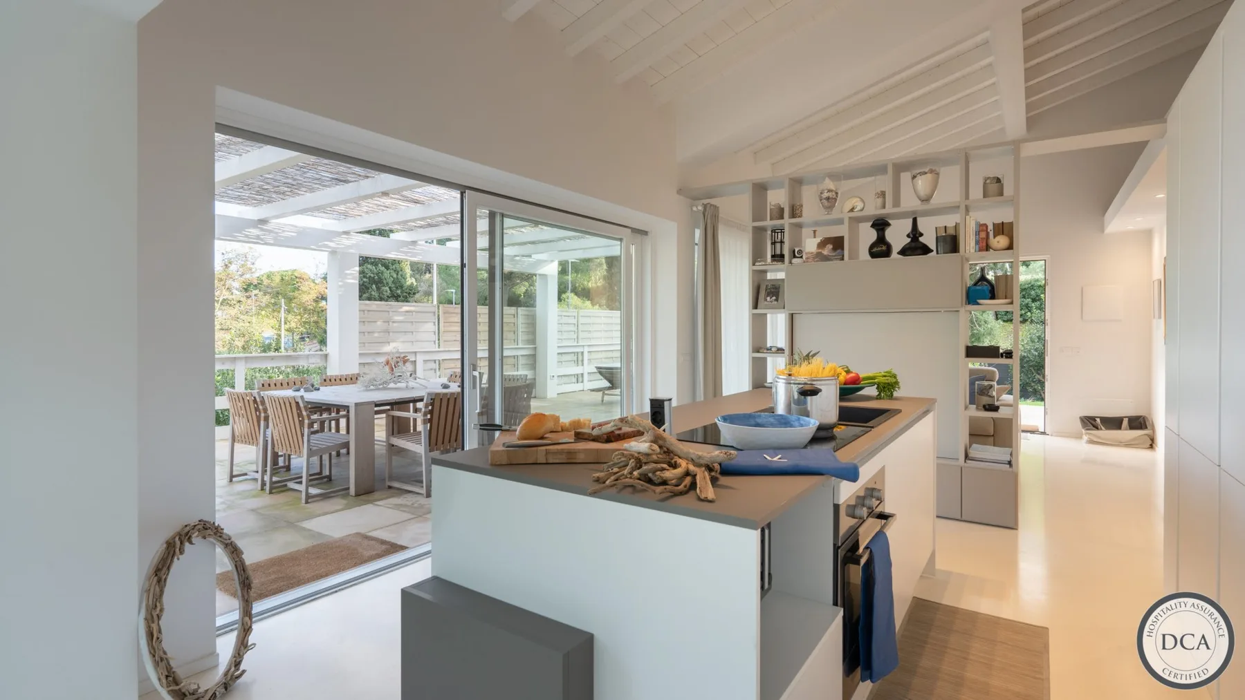 A bright kitchen with a central island opens onto a glass-enclosed dining area.