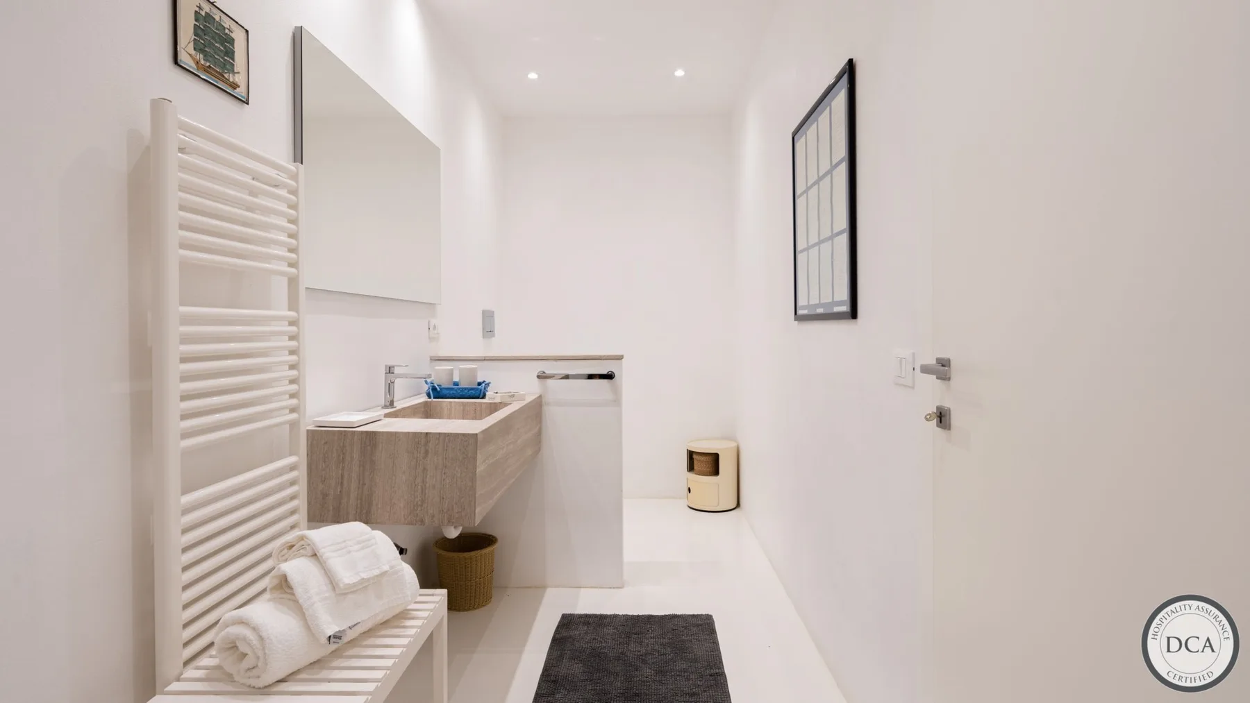 A bright bathroom with a sink, wall-mounted towel rack, and dark floor mat.