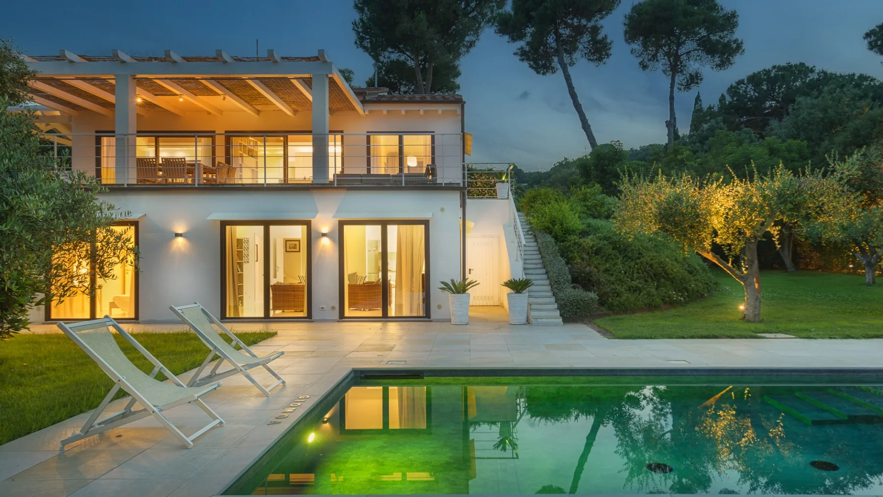 A modern house opens onto a swimming pool, with outdoor lounge chairs on the patio.