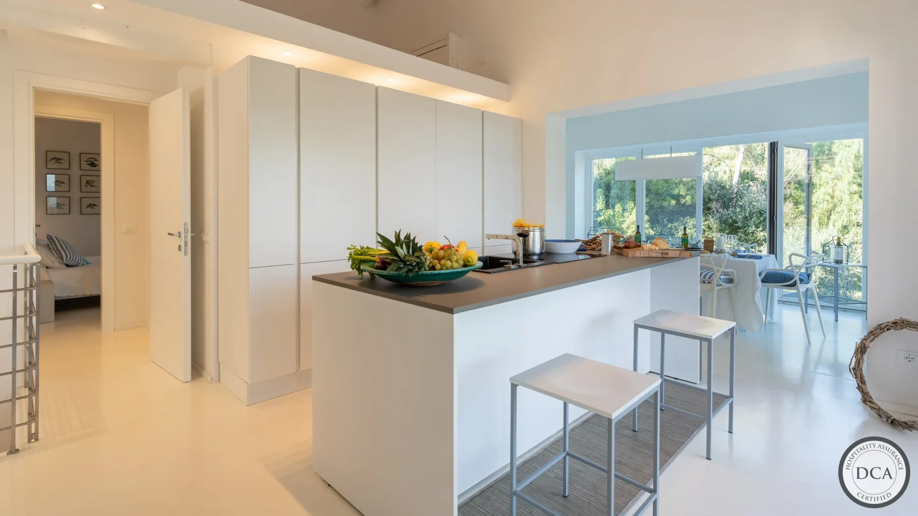 A bright modern kitchen opens onto a dining area with large windows.