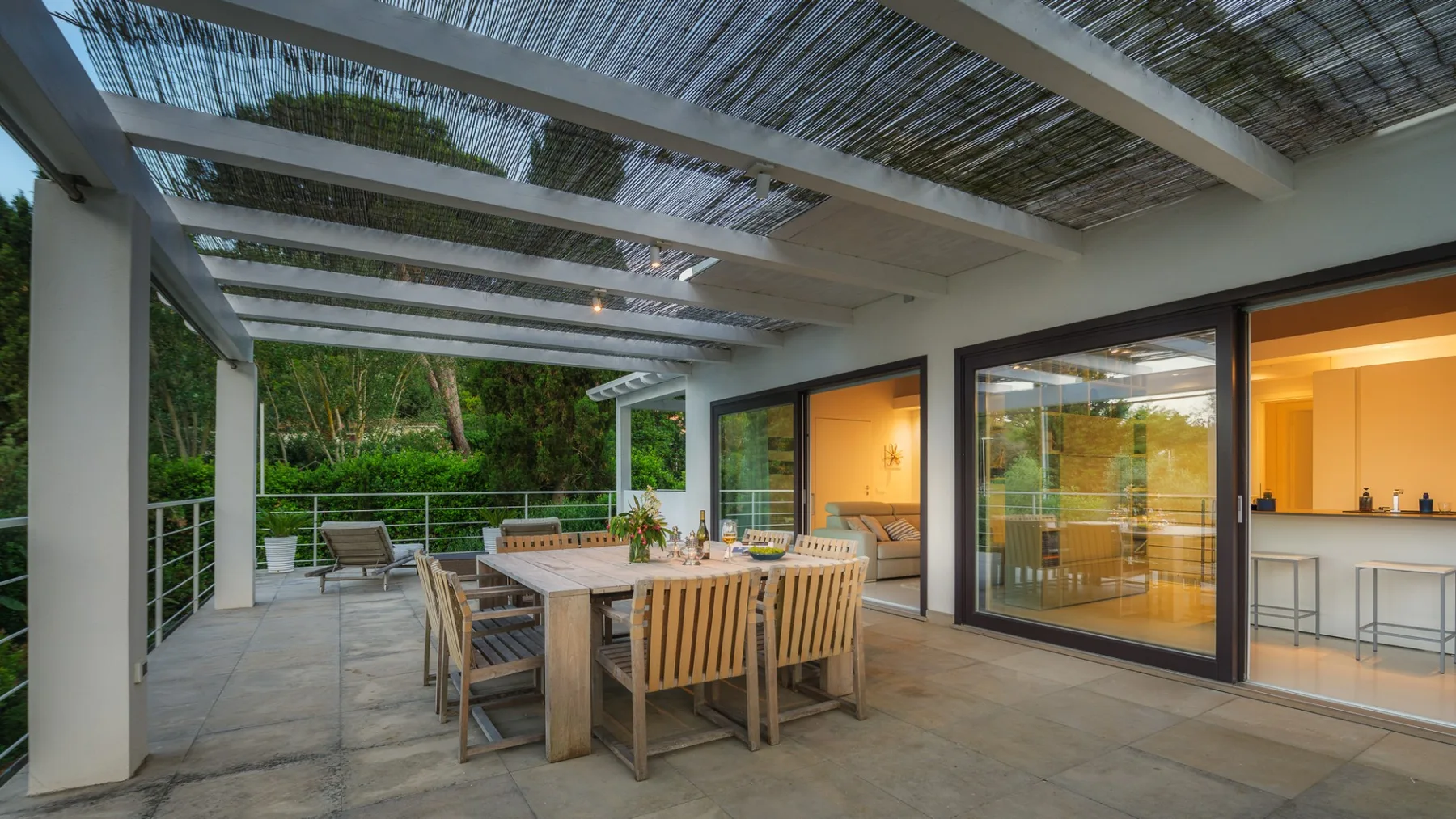 A covered outdoor dining area beside a modern kitchen, with a wooden table and seating.