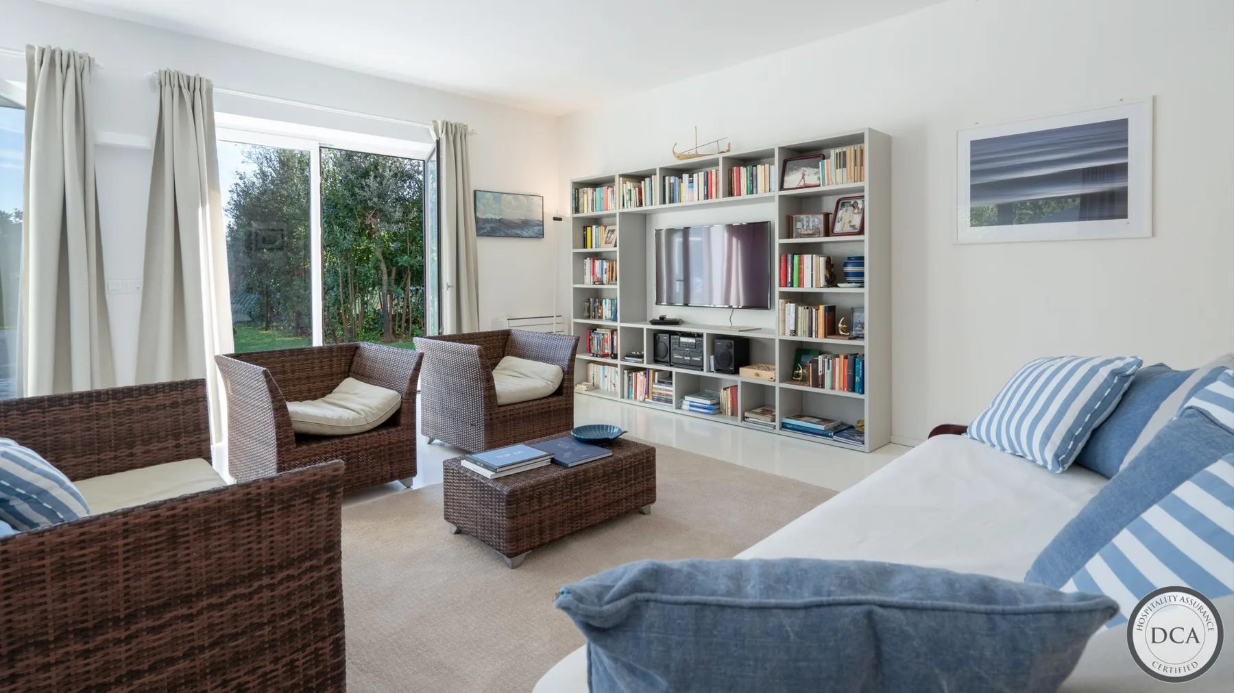 A bright living room with wicker seating, a coffee table, and a wall of bookshelves.