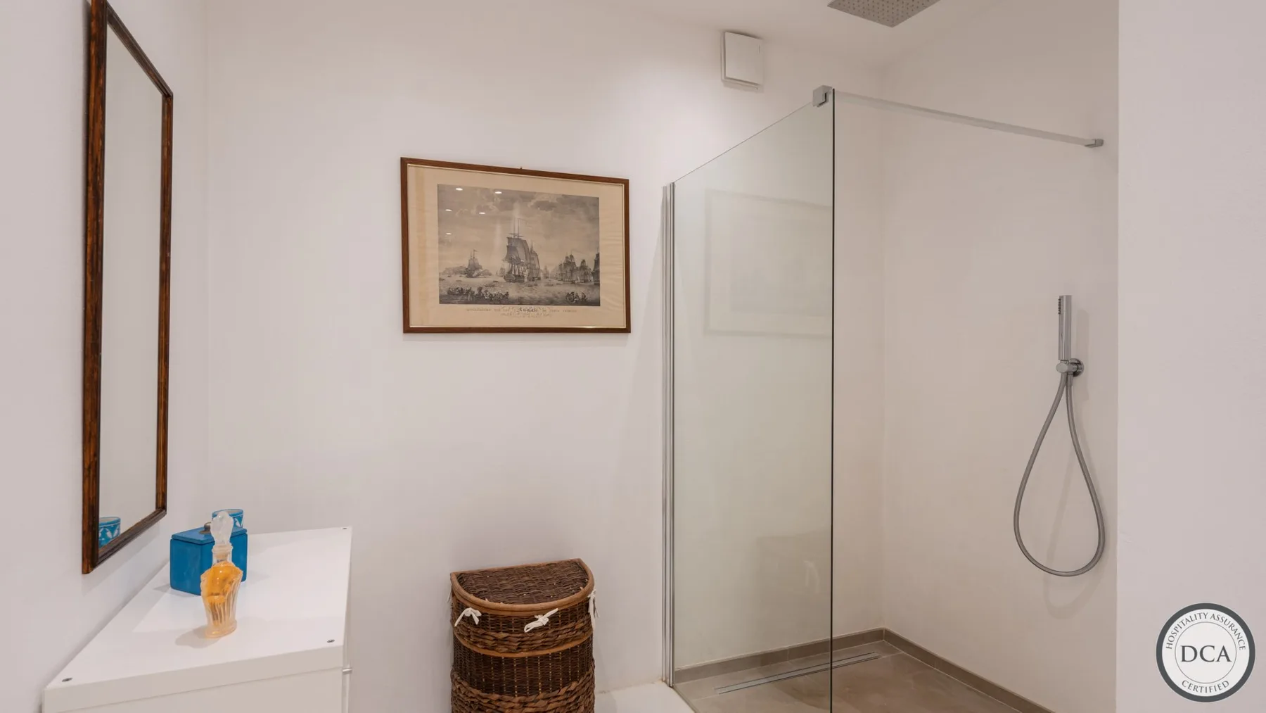 A bathroom with a glass shower, counter, and framed wall art.