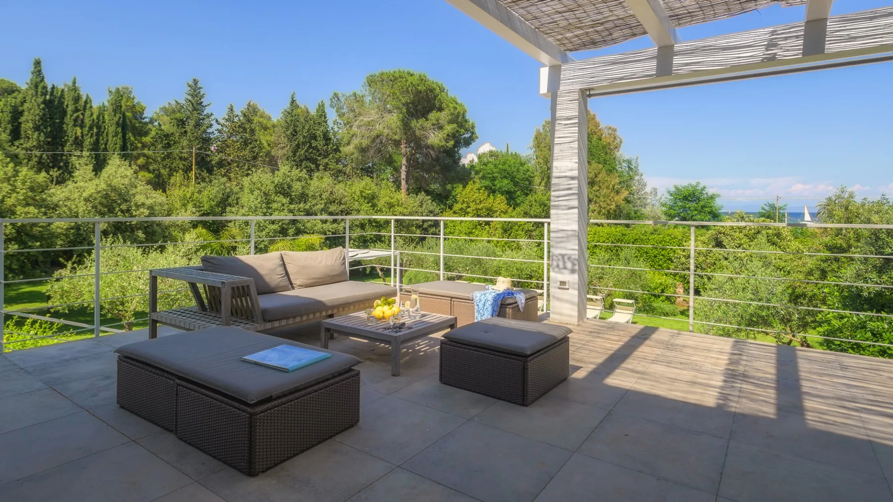 A sunny outdoor terrace with seating and a view of surrounding trees.
