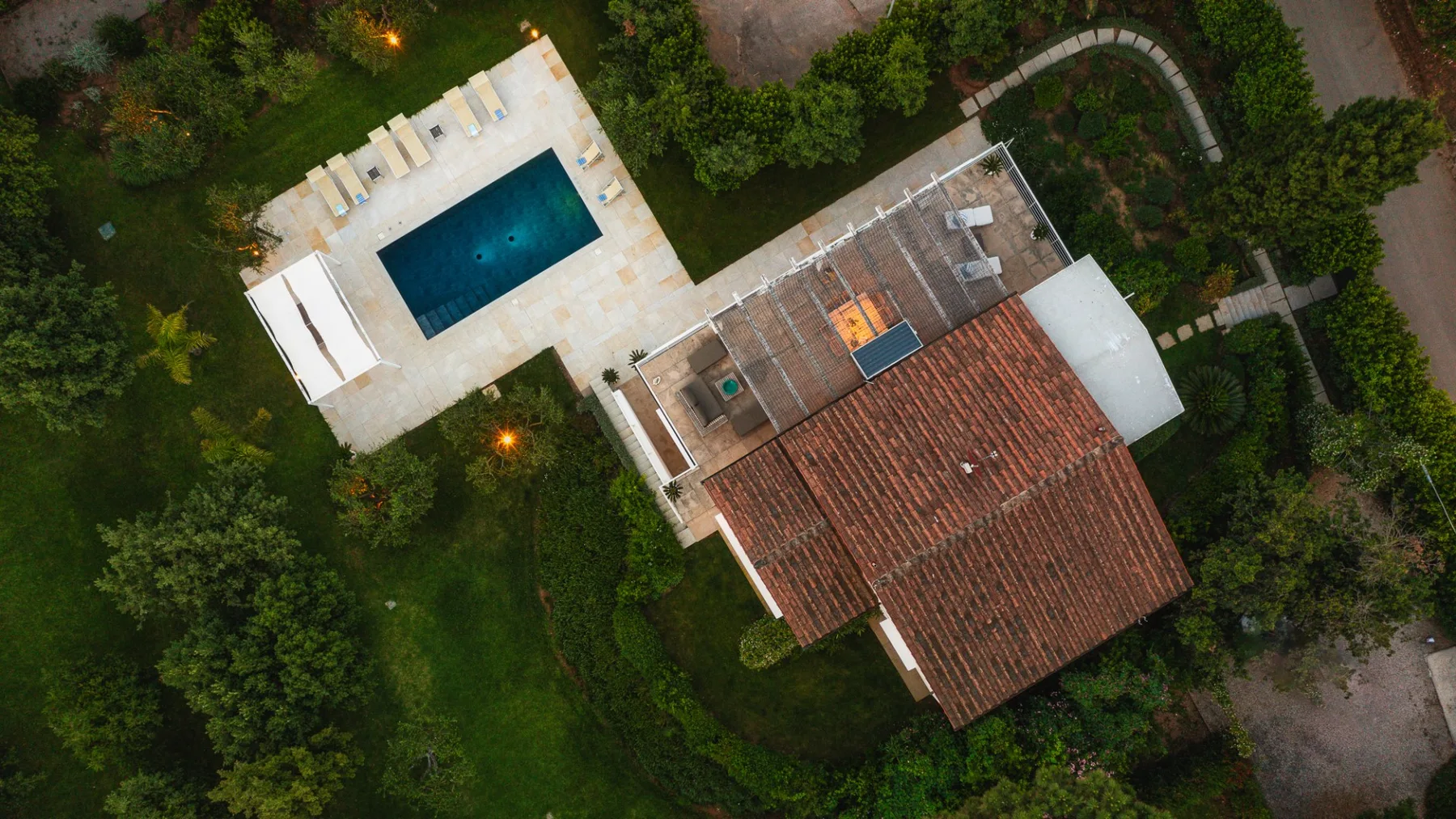 An aerial view of a house with a swimming pool surrounded by greenery.