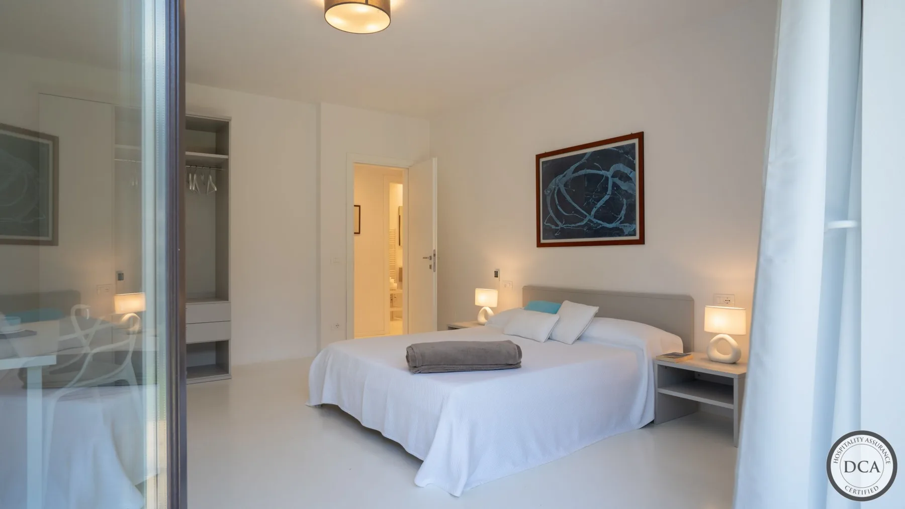 A bright bedroom with a neatly made bed and framed artwork above the headboard.