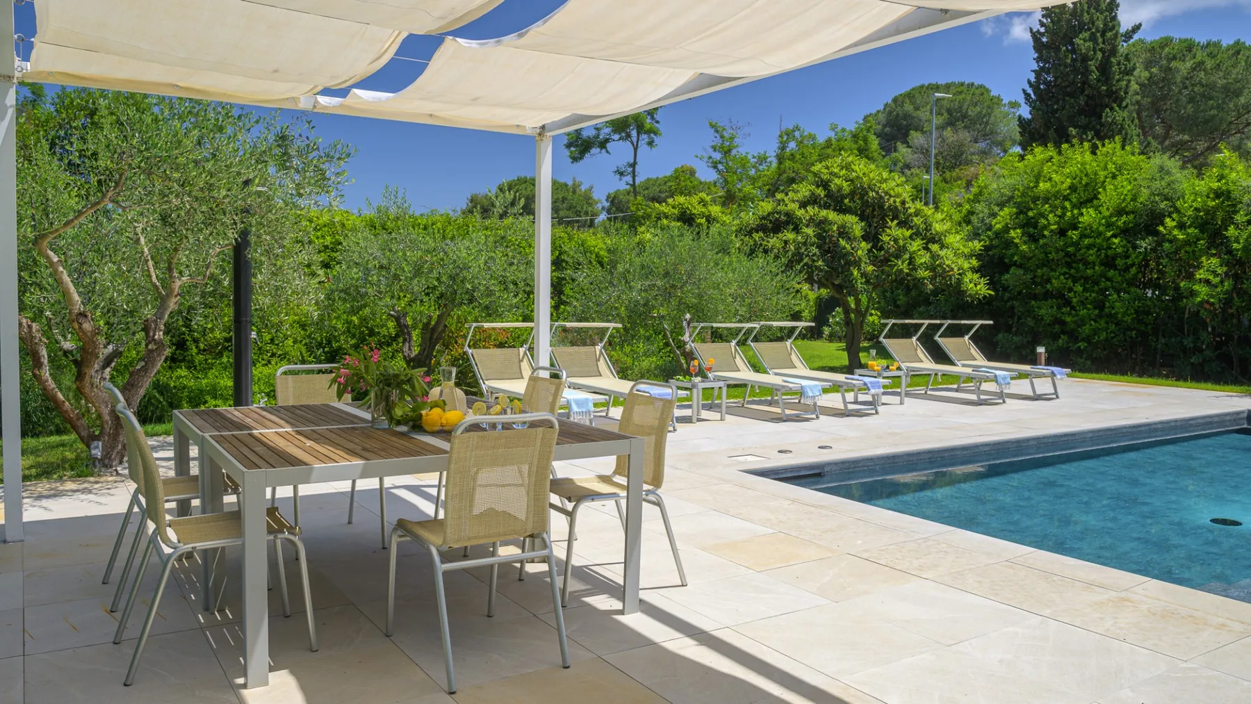 An outdoor dining area and swimming pool sit beside a leafy garden.
