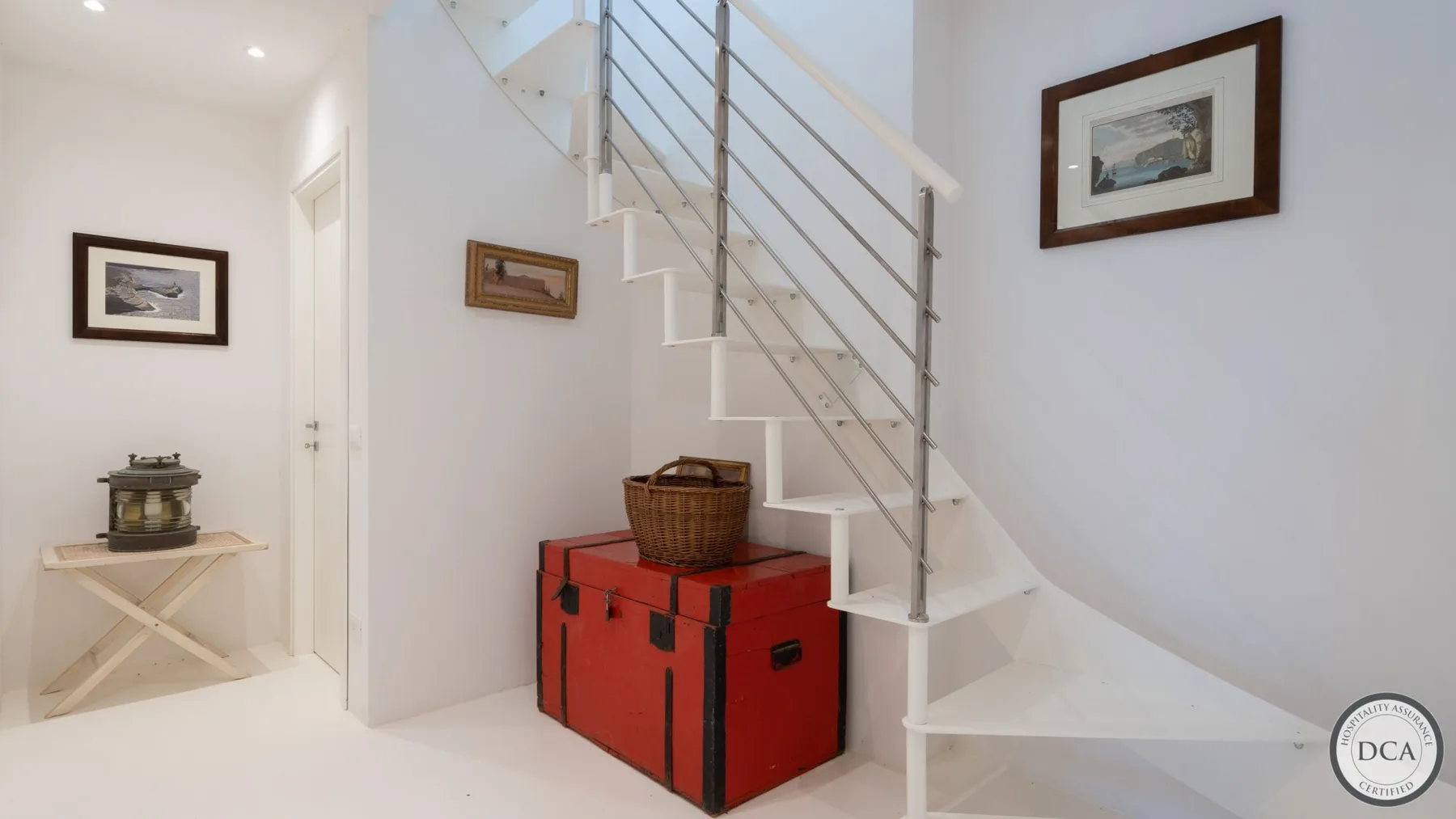 A bright interior hallway with a staircase and a red storage chest beneath it.