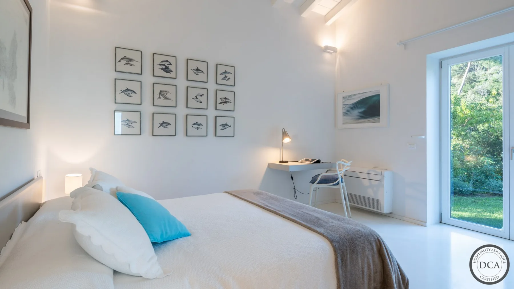 A bright bedroom with a bed, wall art, and a glass door opening to greenery.