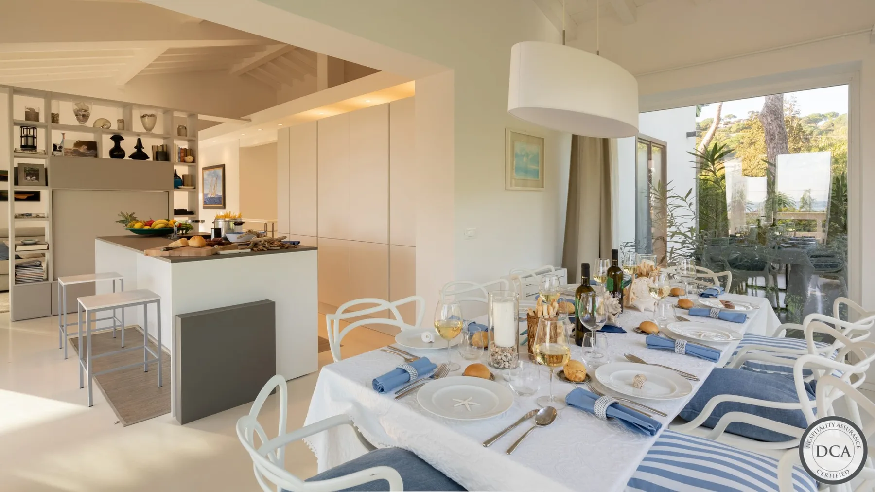 A bright dining area with a long table set for a meal beside the kitchen.