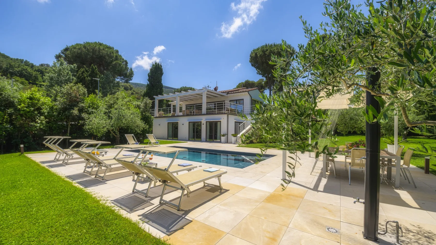 A modern villa with a swimming pool, sun loungers, and a landscaped garden.