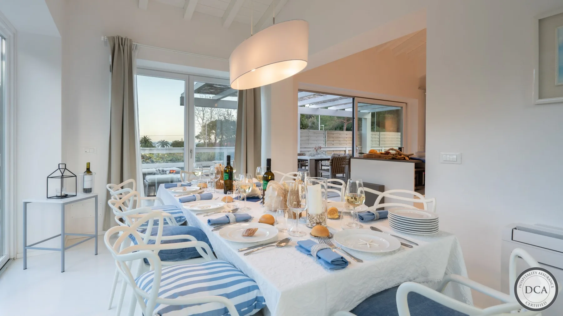 A dining area with a long table set with dishes beside large windows.