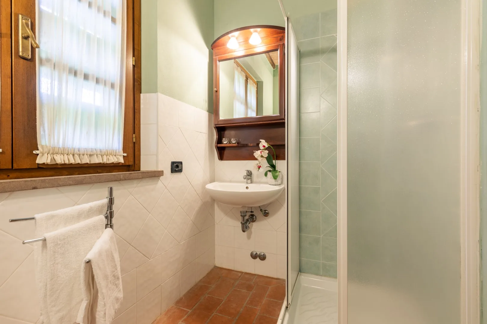 A bathroom with a wall-mounted sink, mirror, and glass shower.