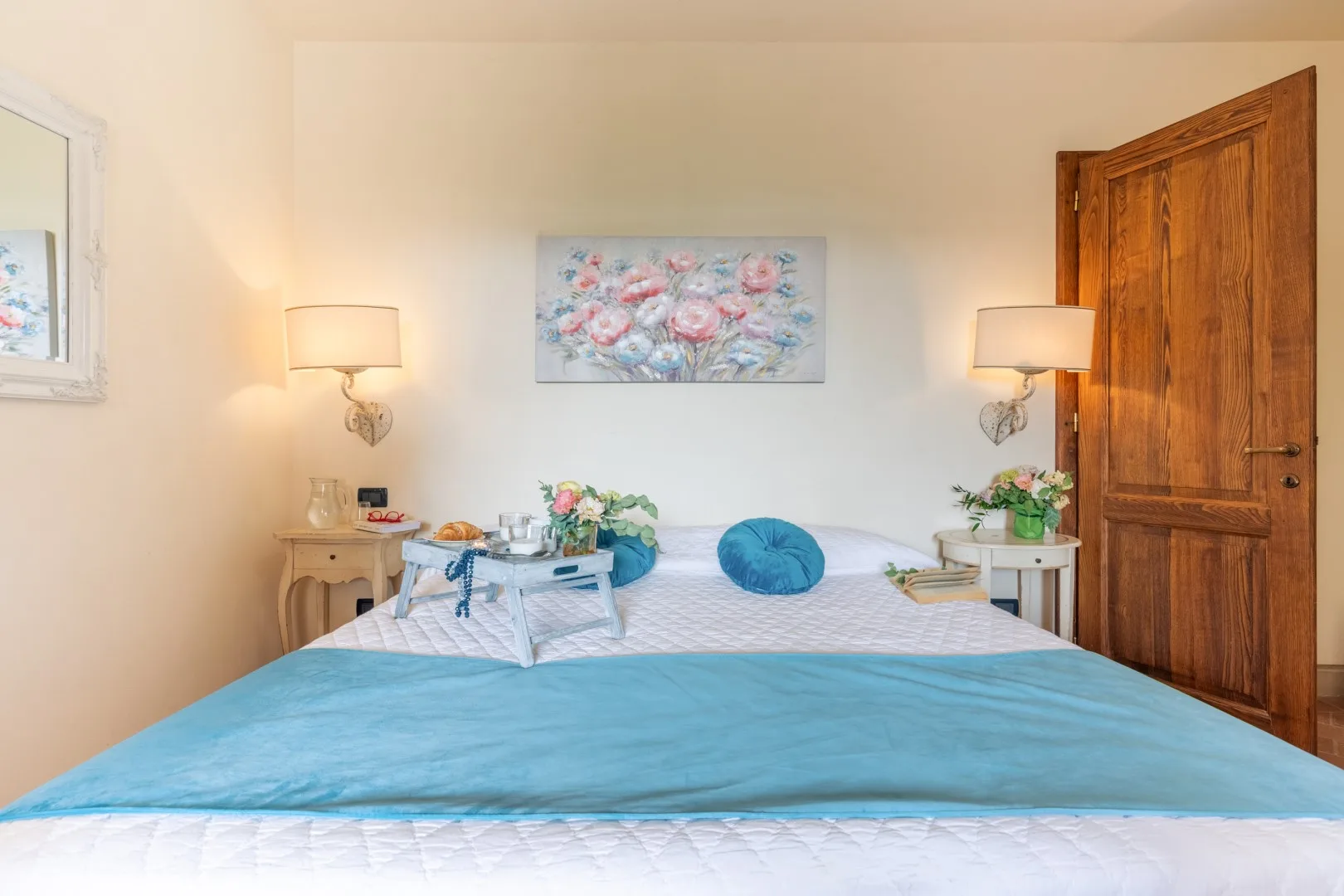 Bedroom with a bed beneath floral artwork and bedside lamps.