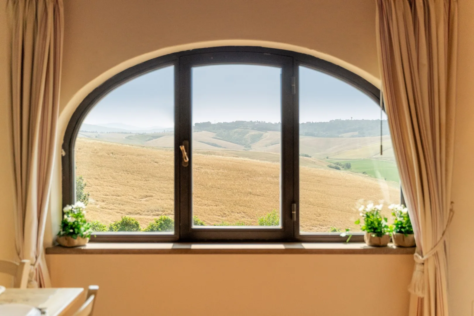 A room with a large arched window overlooking fields and rolling hills.