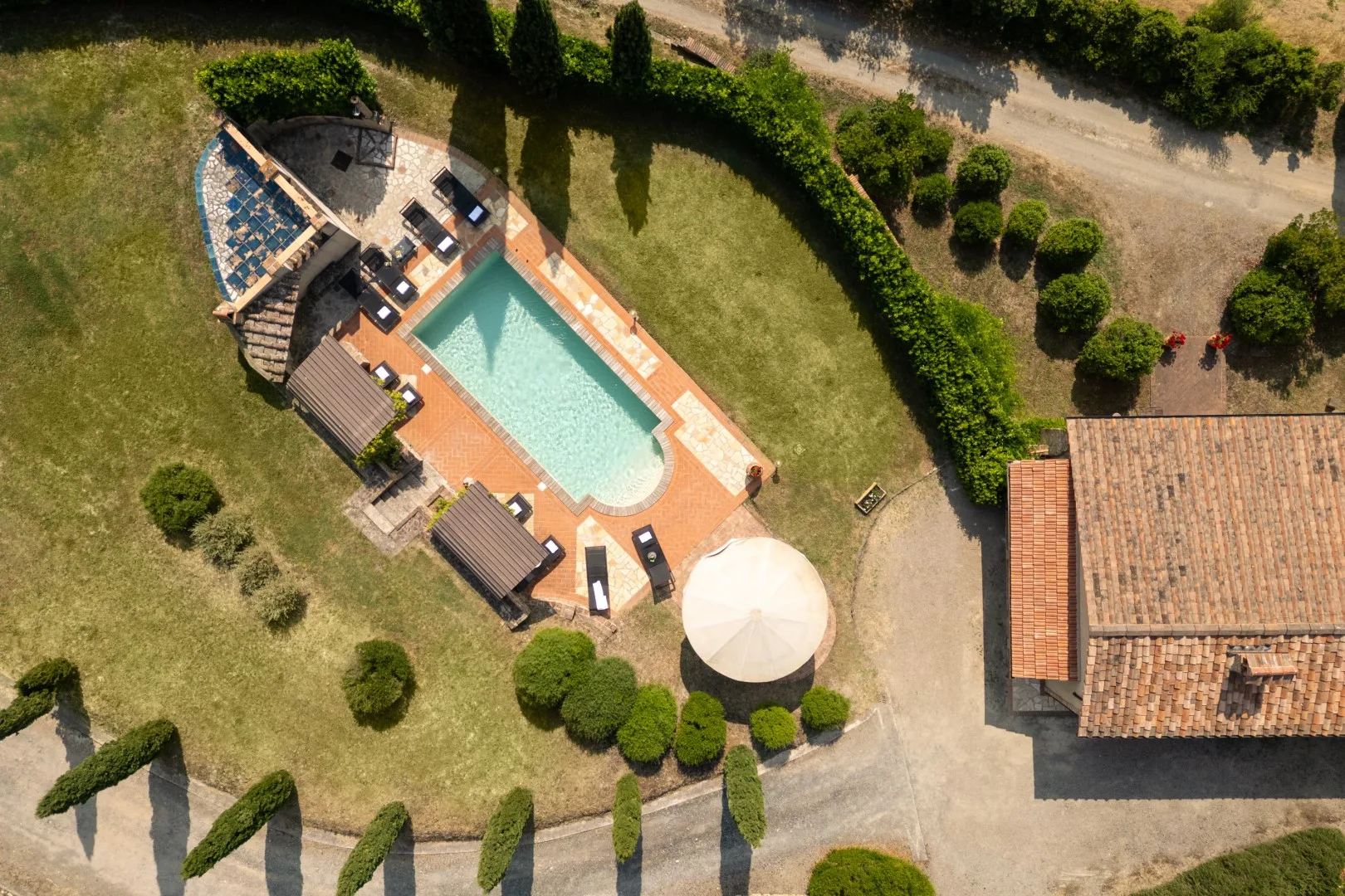 An aerial view of a swimming pool and surrounding lawn, with a shaded seating area.