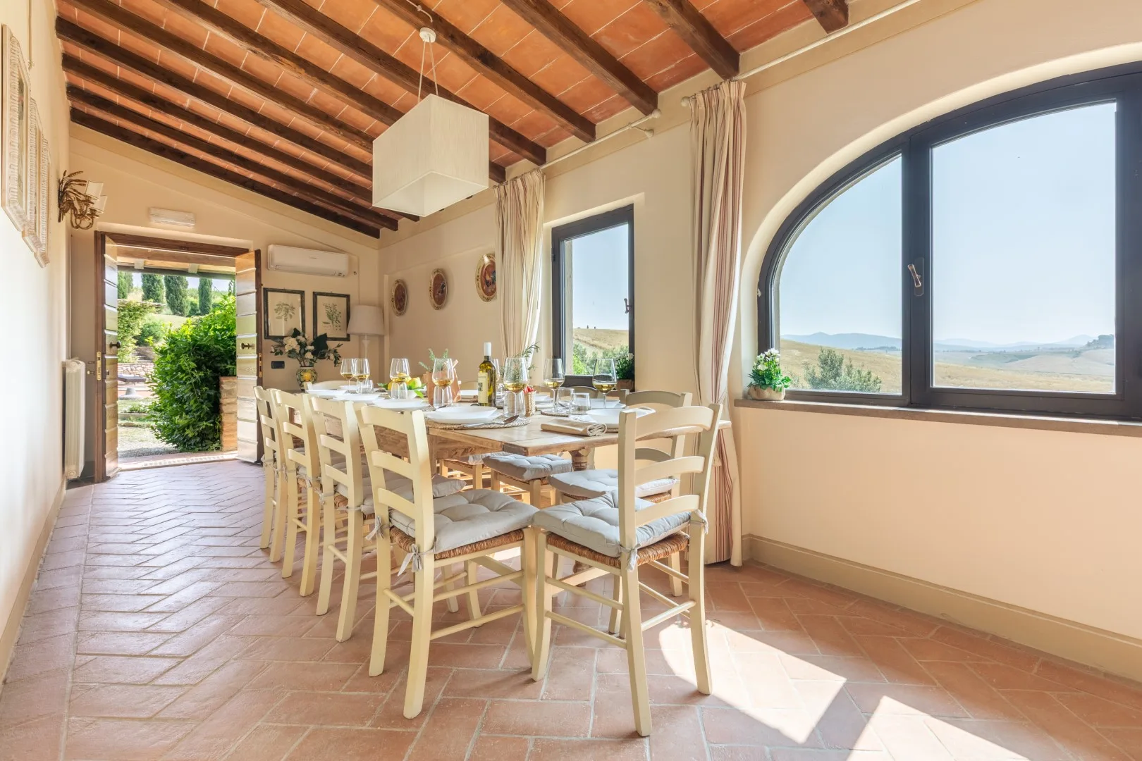 A dining room with a long table and chairs beside a large arched window.