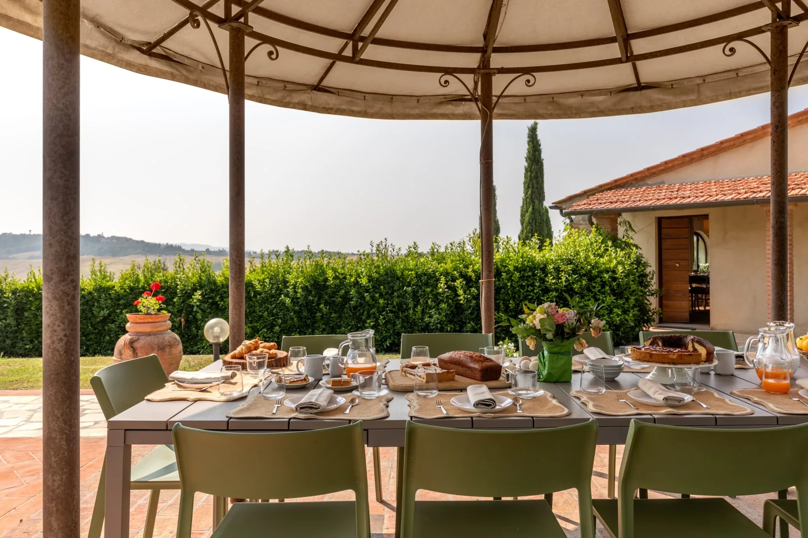 An outdoor dining area is set beneath a canopy beside a garden.
