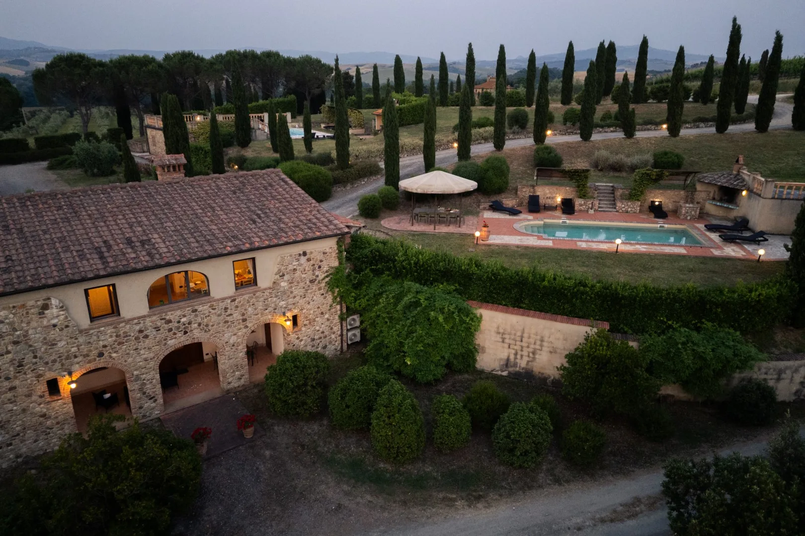 A stone villa and outdoor swimming pool sit among gardens and tall trees.