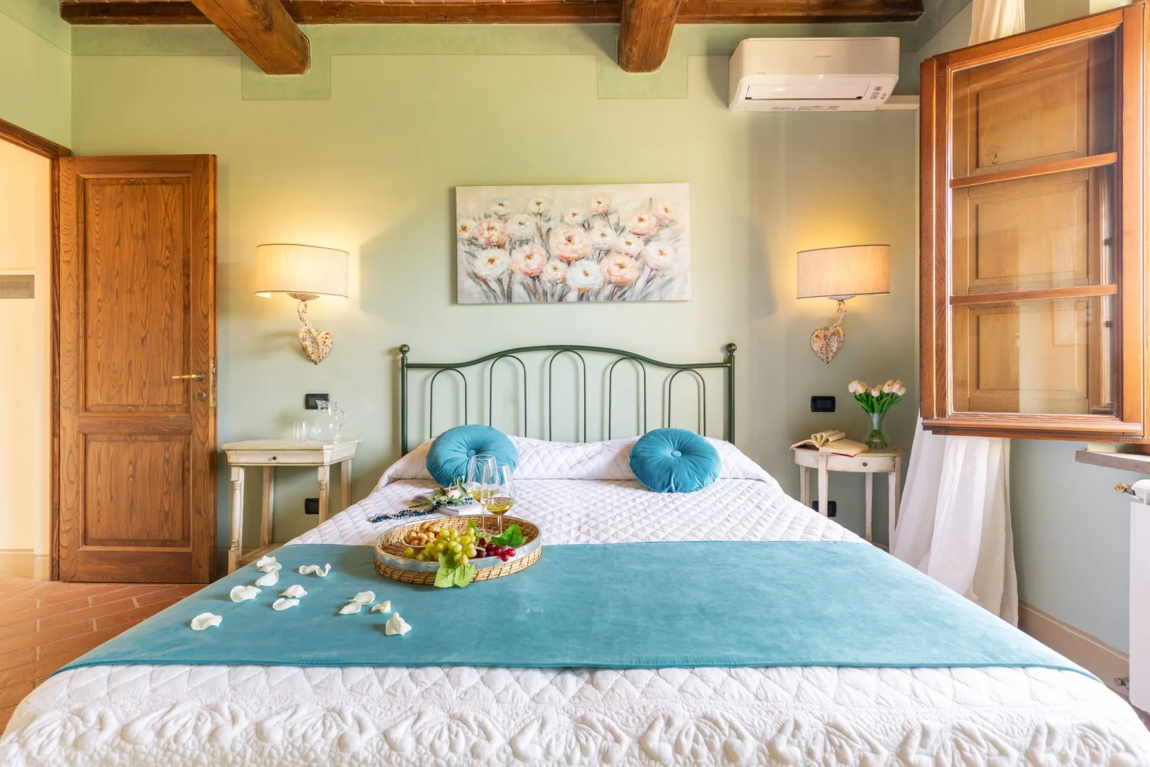 A bedroom with a bed beneath floral artwork and beside a wooden window.