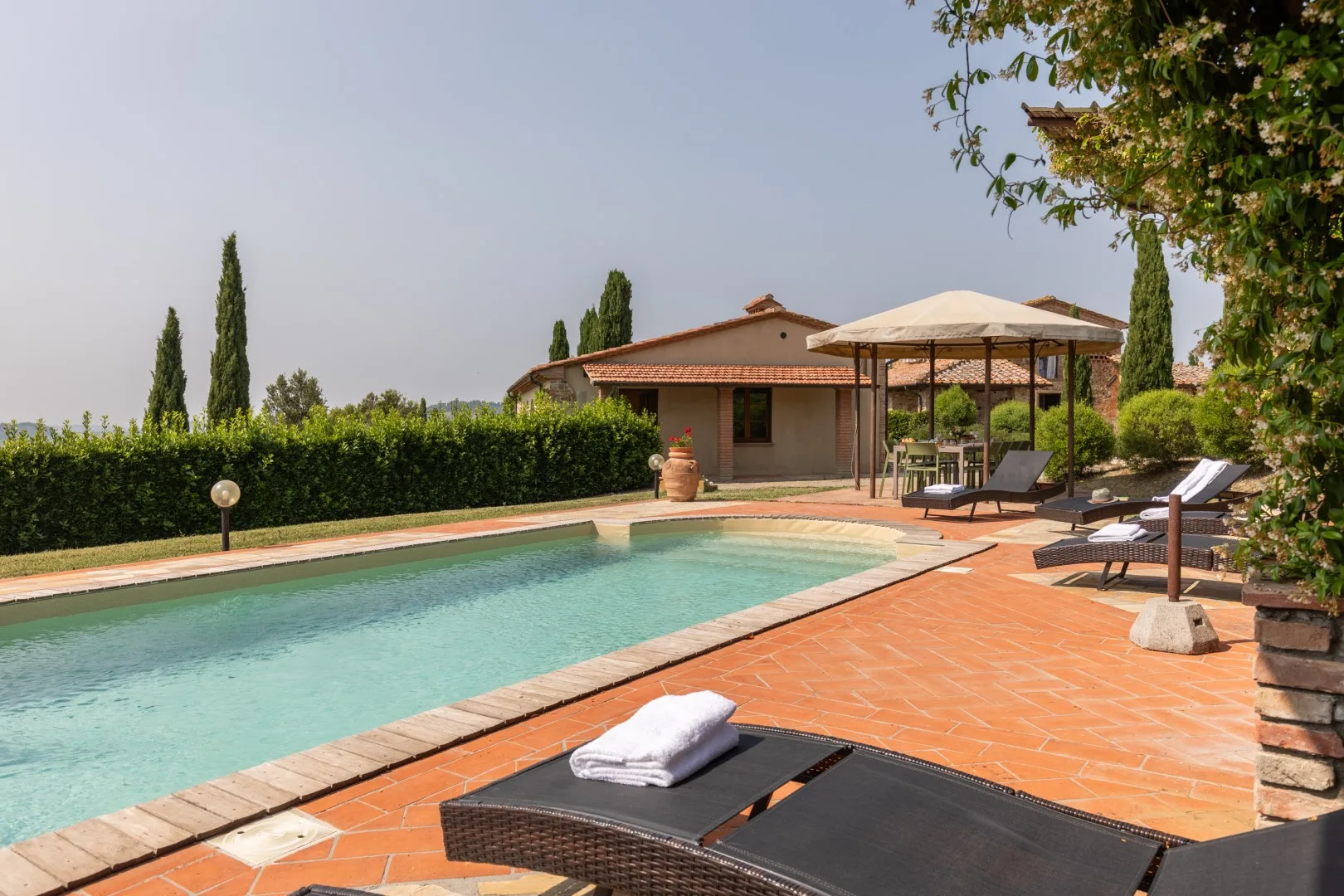 An outdoor swimming pool beside a terracotta-tiled patio with loungers.